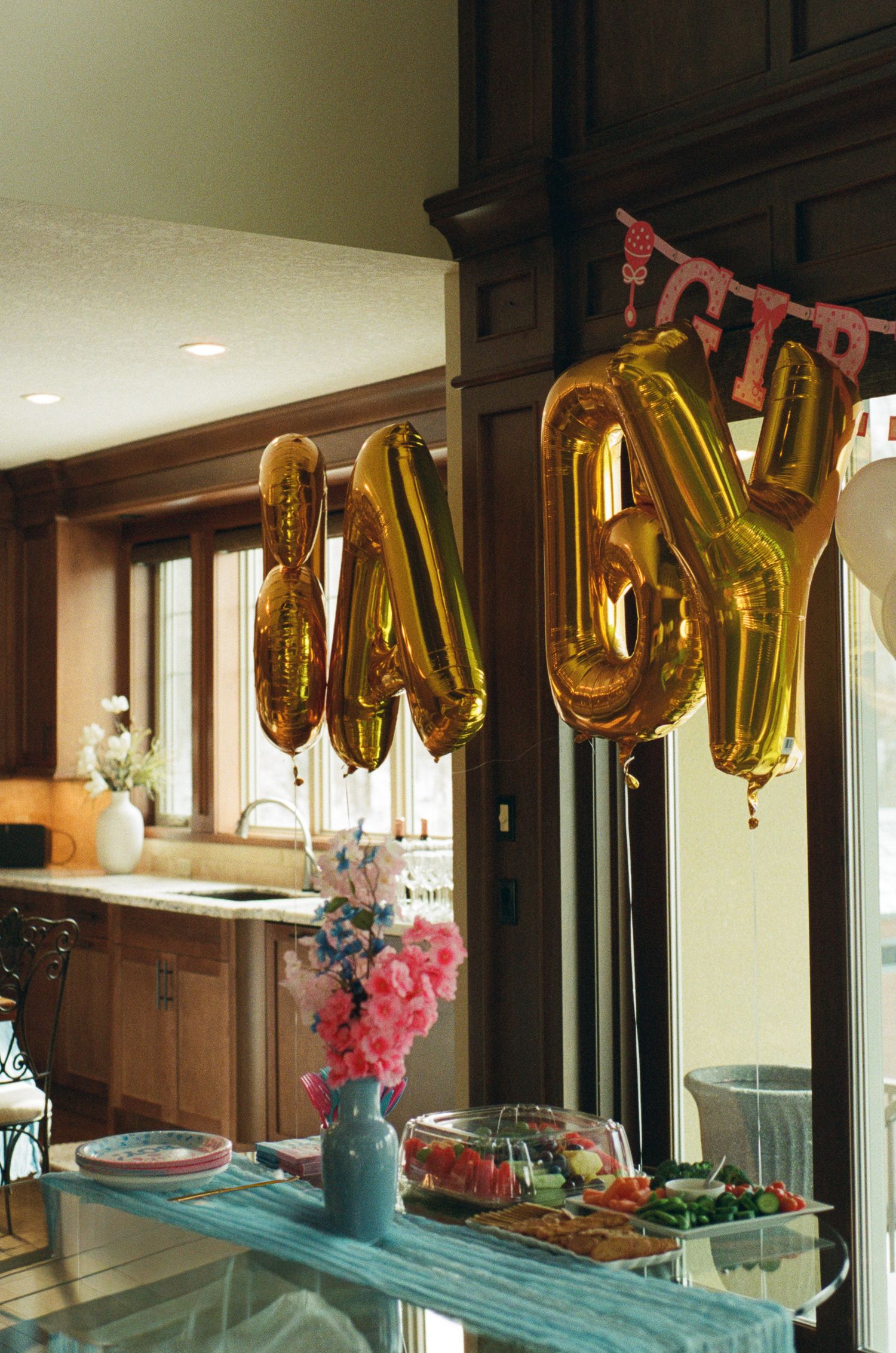 Gold BABY letter balloons hanging above a decorated baby shower party table in a modern kitchen.