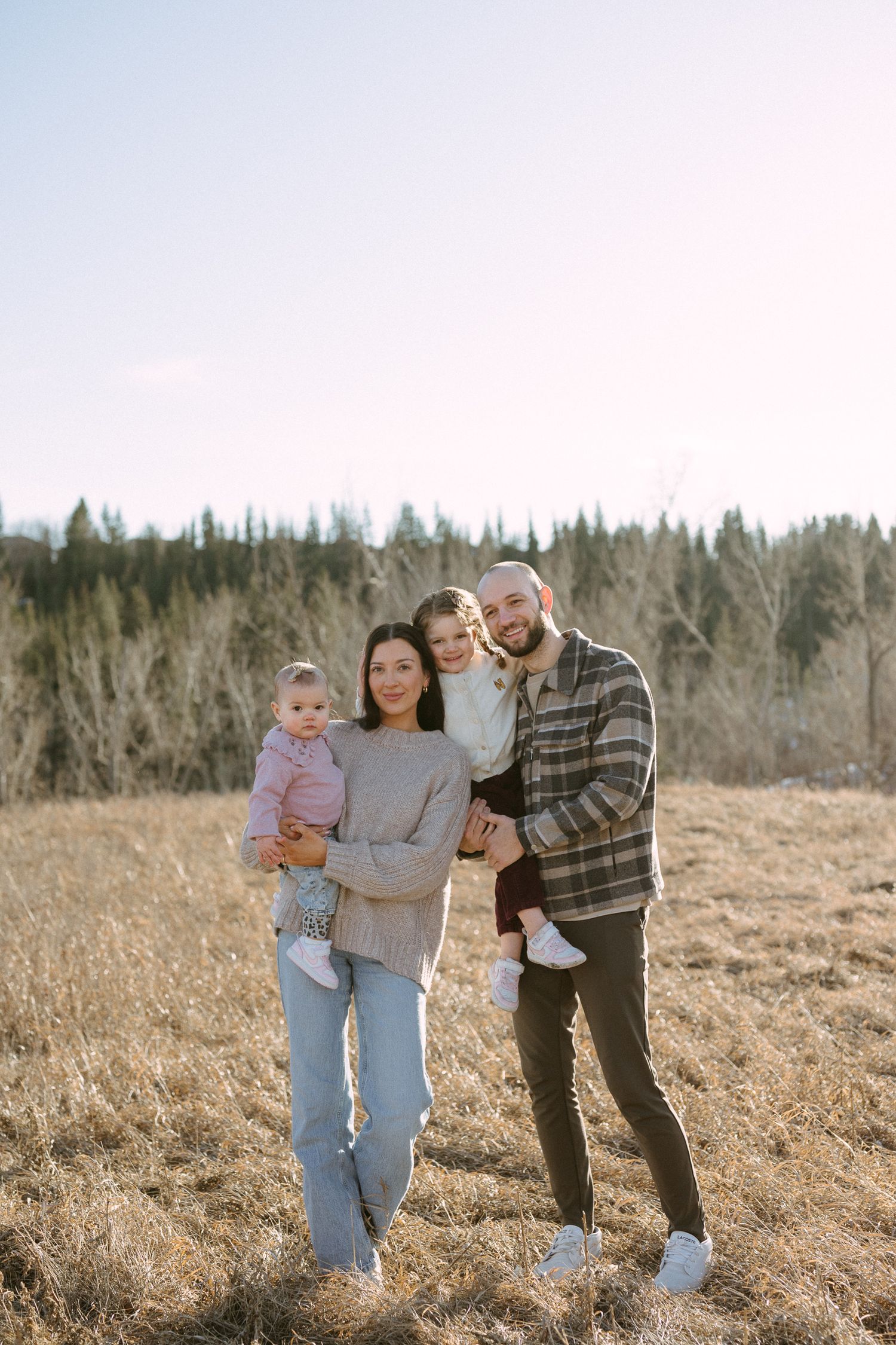 Family enjoying time together outdoors in a field with evergreen trees in the background on a sunny day.
