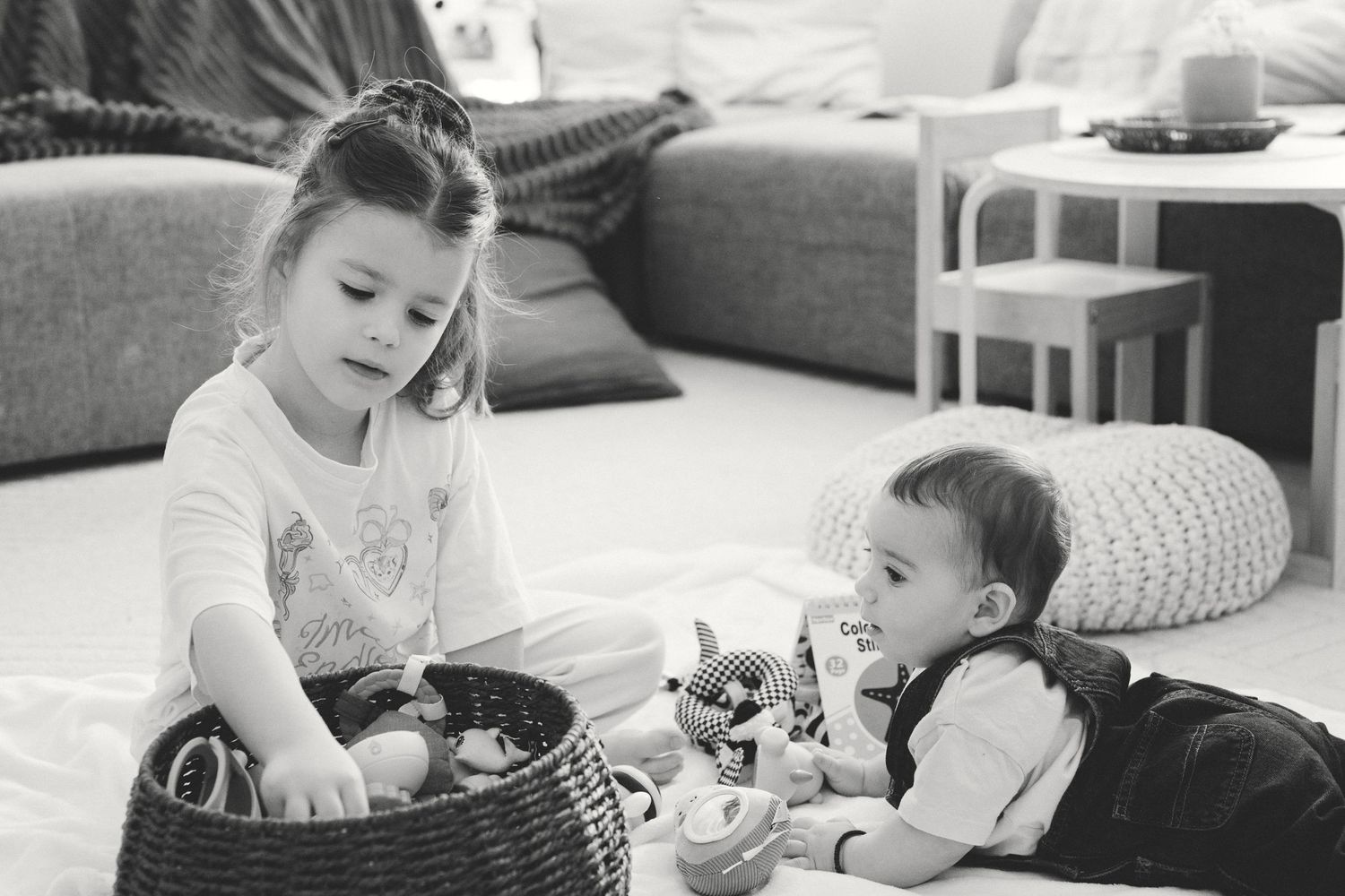 Two children playing together with toys in a basket on the living room floor.