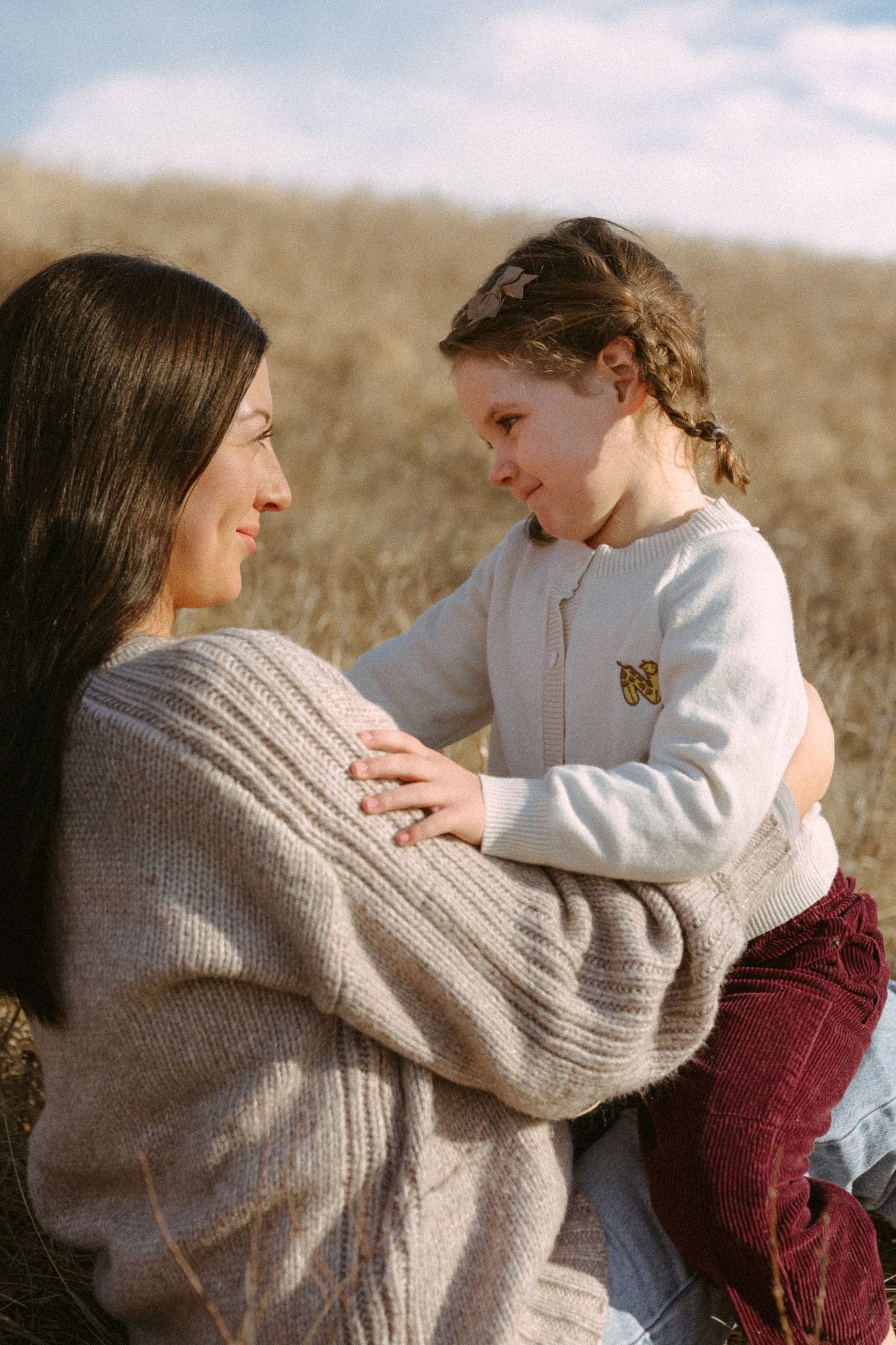 A tender moment shared between two people sitting in a golden field wearing cozy sweaters on a sunny day.