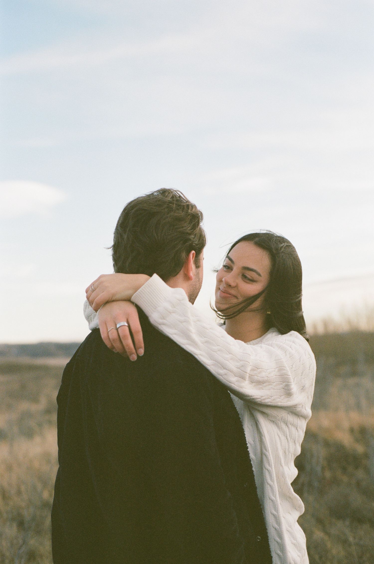 A romantic embrace captured in a field during golden hour with soft lighting.
