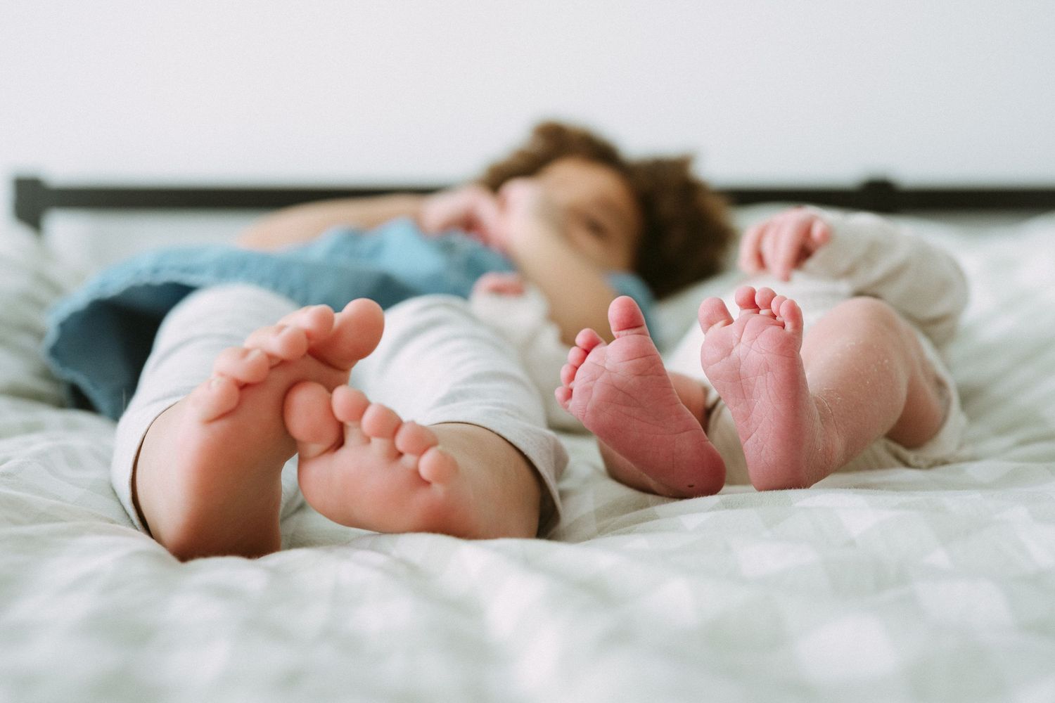 Close-up of toddler and newborn baby feet lying on a white bed together.