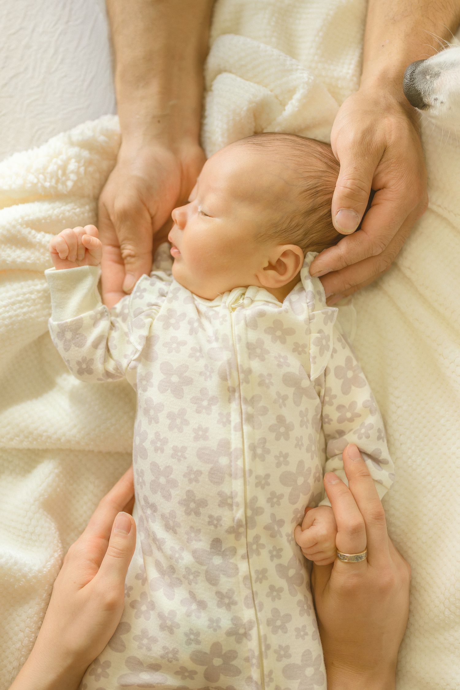 Hands gently dressing a young baby in floral clothing on white bedding.