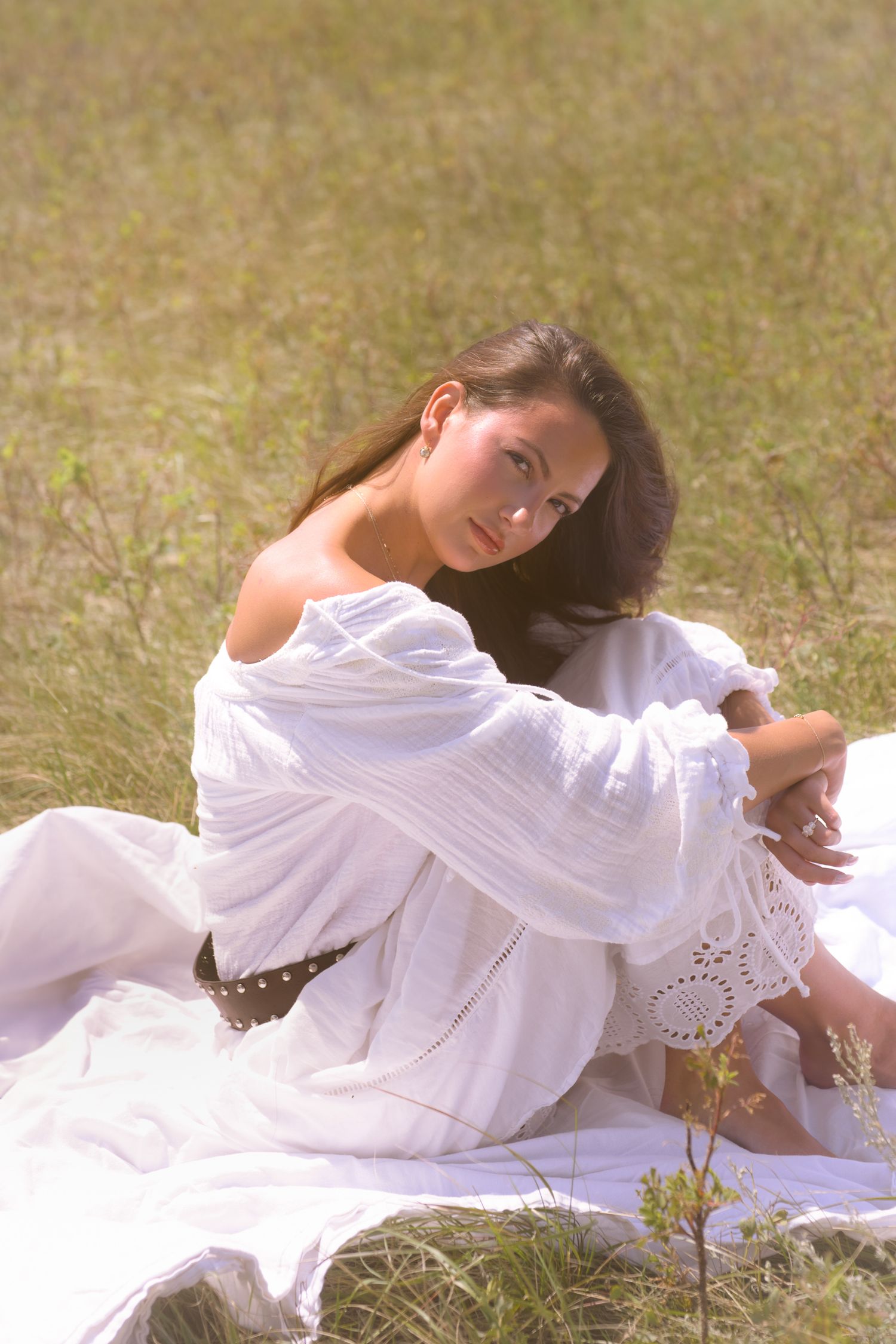 A flowing white dress creates graceful movement against golden grass in an artistic outdoor portrait.