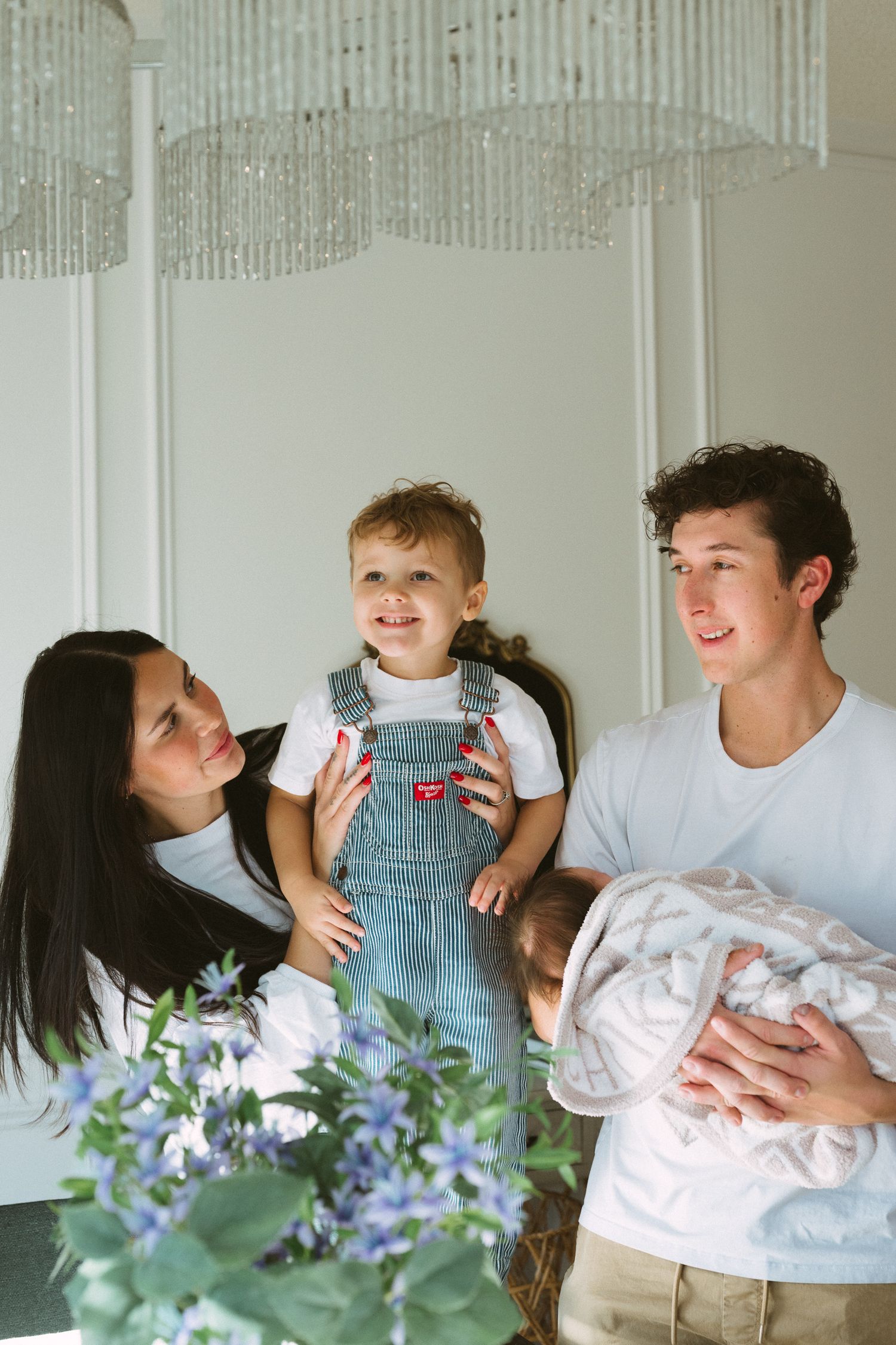 A tender family moment showing affection with a baby in striped overalls against a light background with blue flowers.