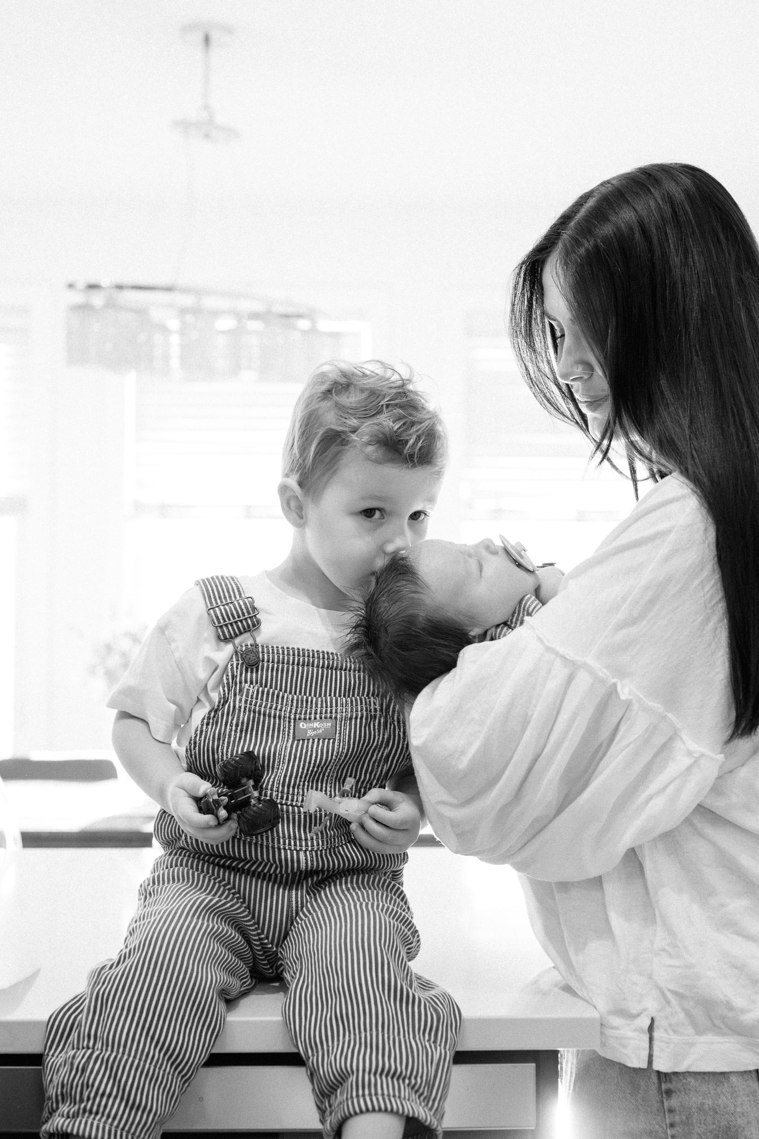 Black and white photo series showing a toddler in striped overalls sitting on a bench with someone in white.