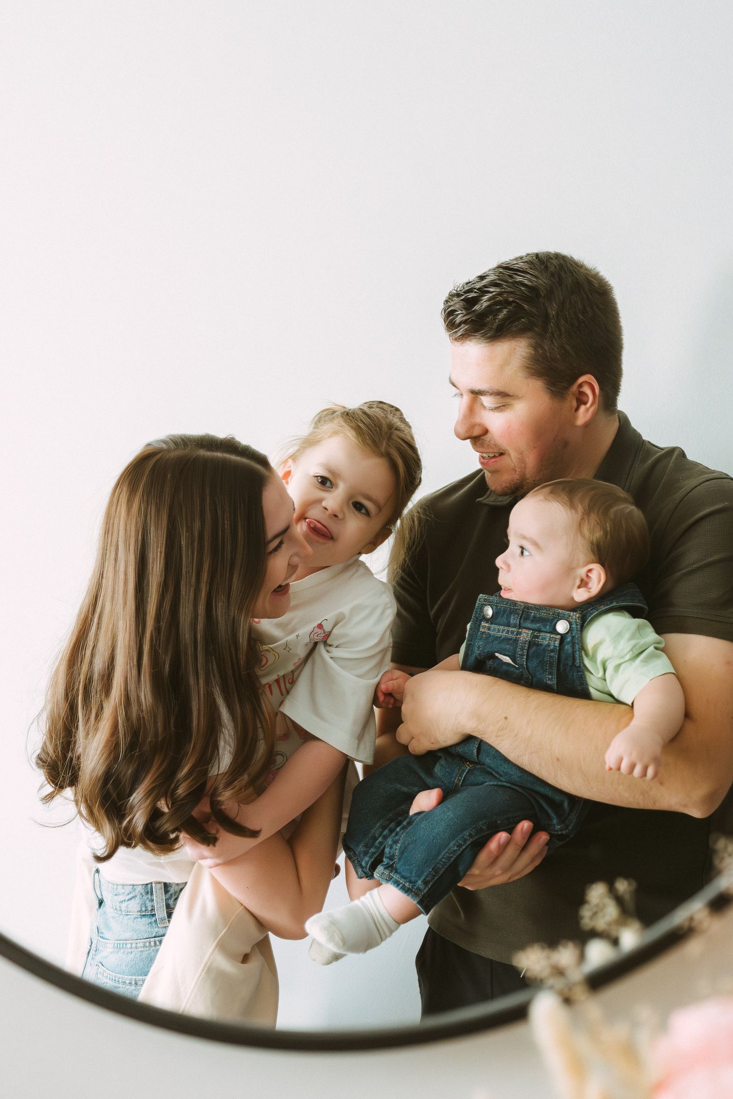 A loving family moment captured in a mirror reflection showing parents with two young children sharing smiles and laughter.