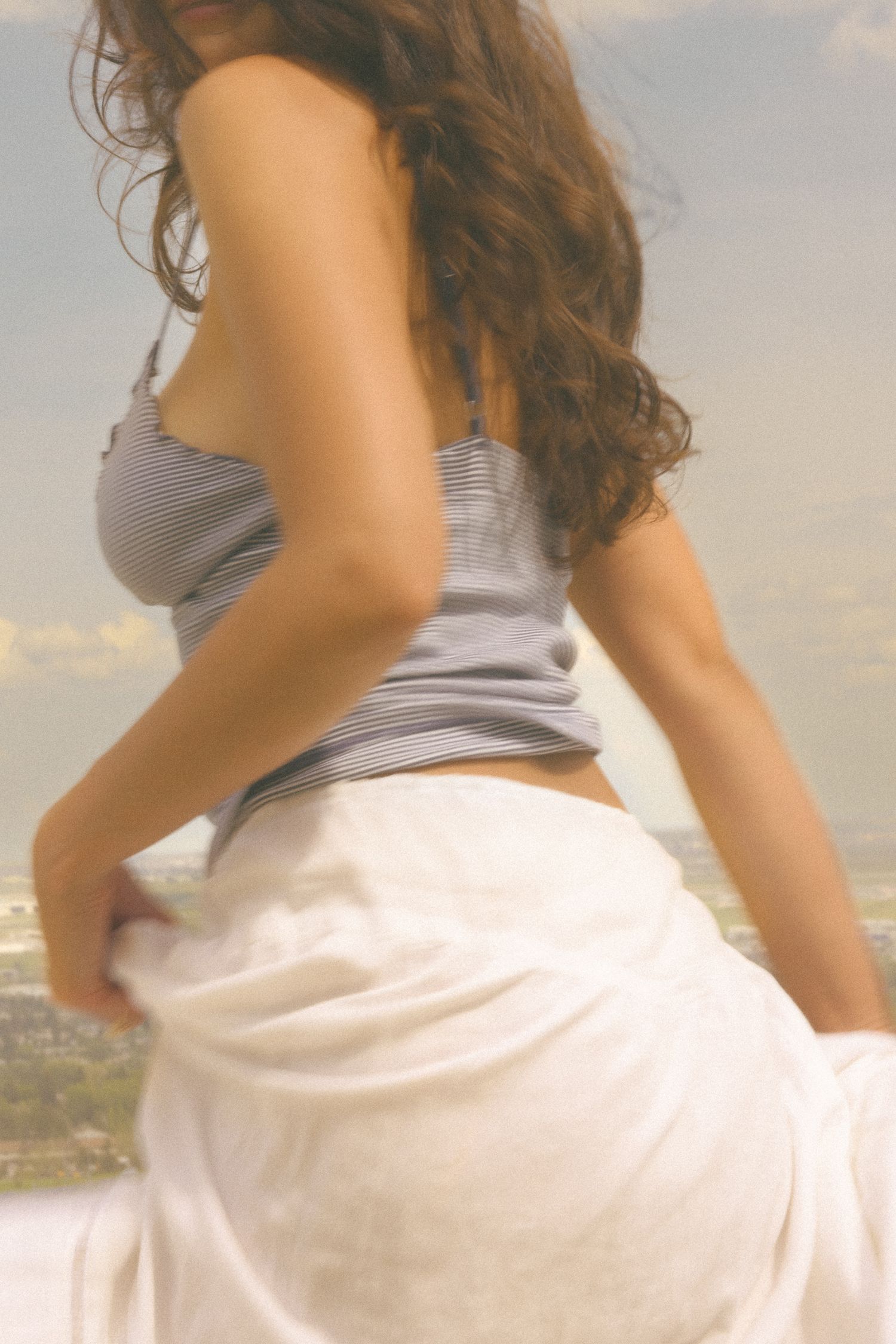 A person in a flowing white skirt and gray top poses outdoors.