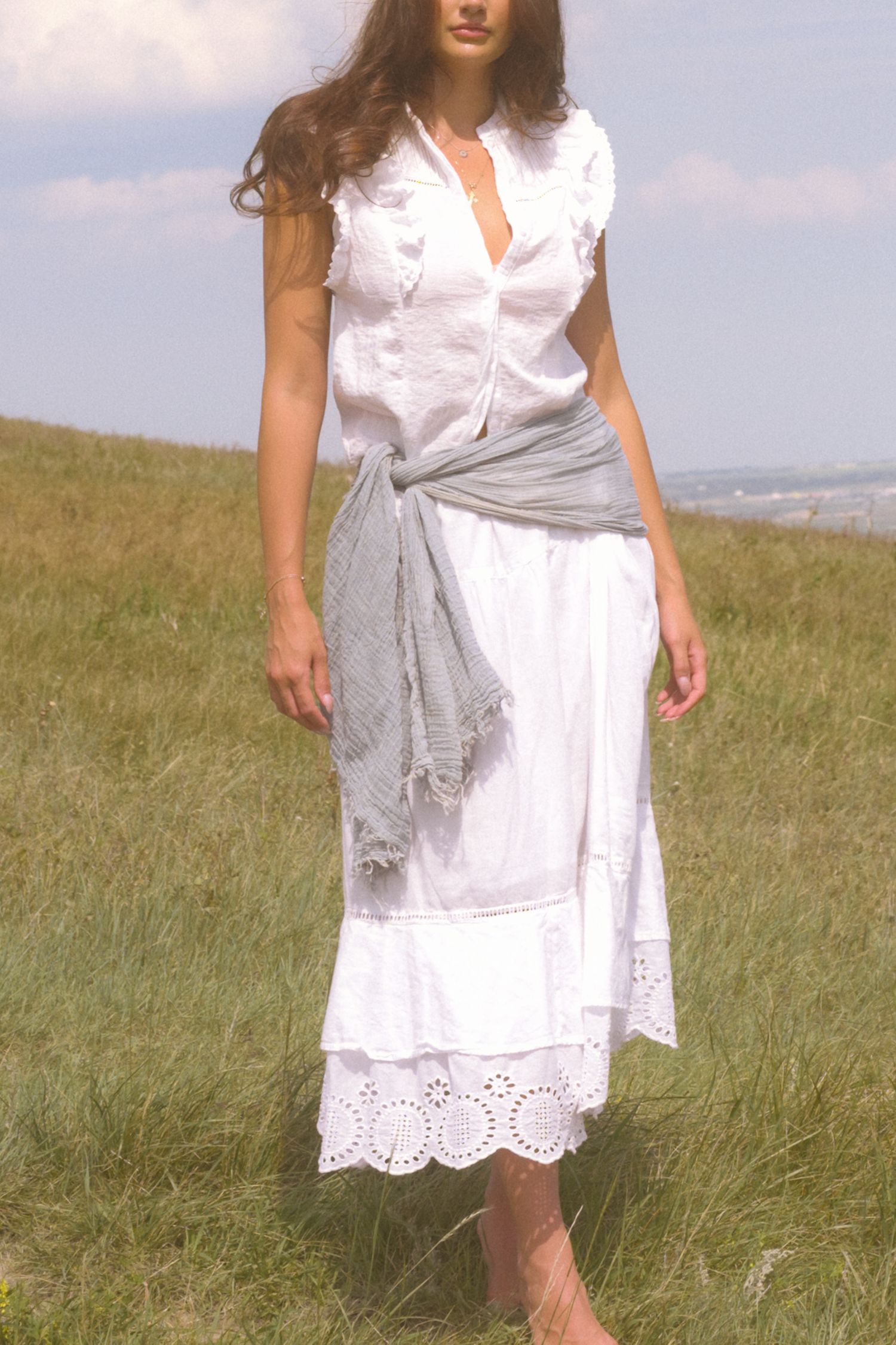 Elegant white dress with grey wrap and eyelet lace hem photographed on a grassy hill.