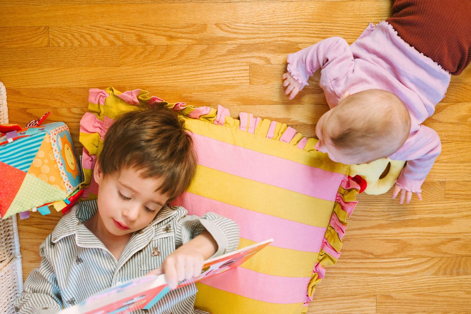 Children playing on wooden floor with pink and yellow striped cushions.