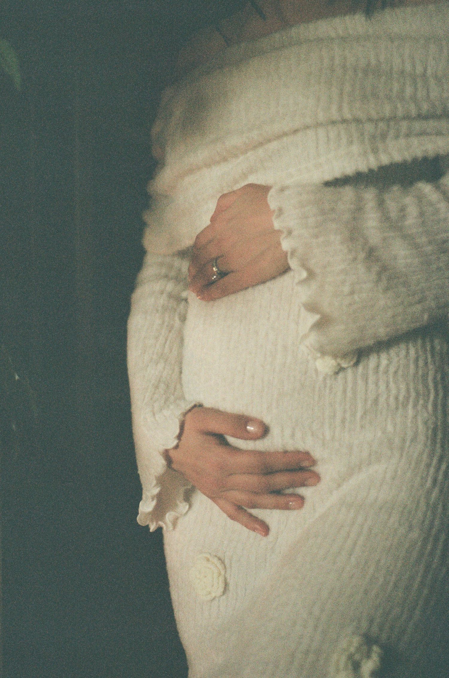 Close-up of pregnant woman in white textured knit outfit gently holding her baby bump with both hands.