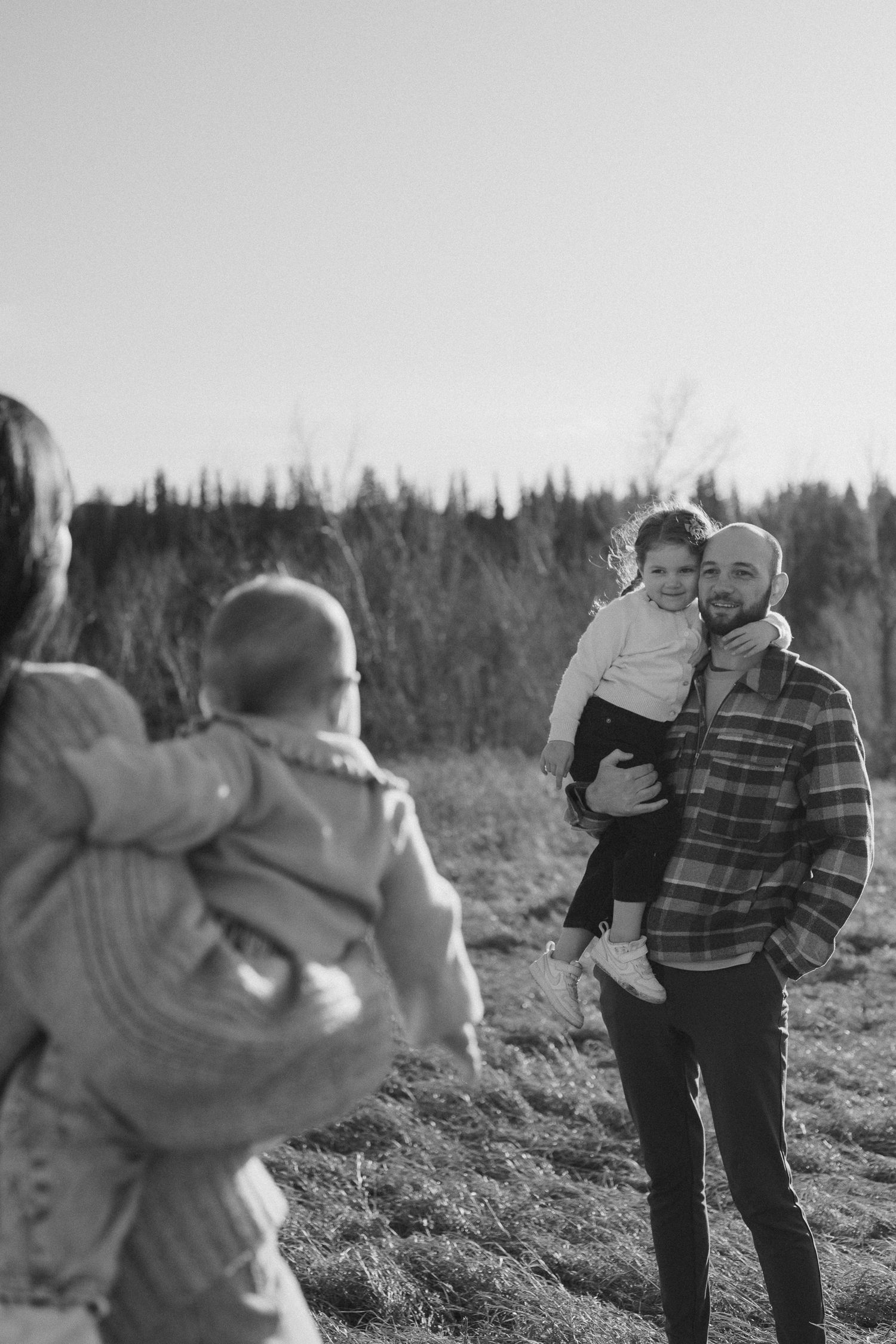 Black and white photo of a family spending time together outdoors with trees in the background.