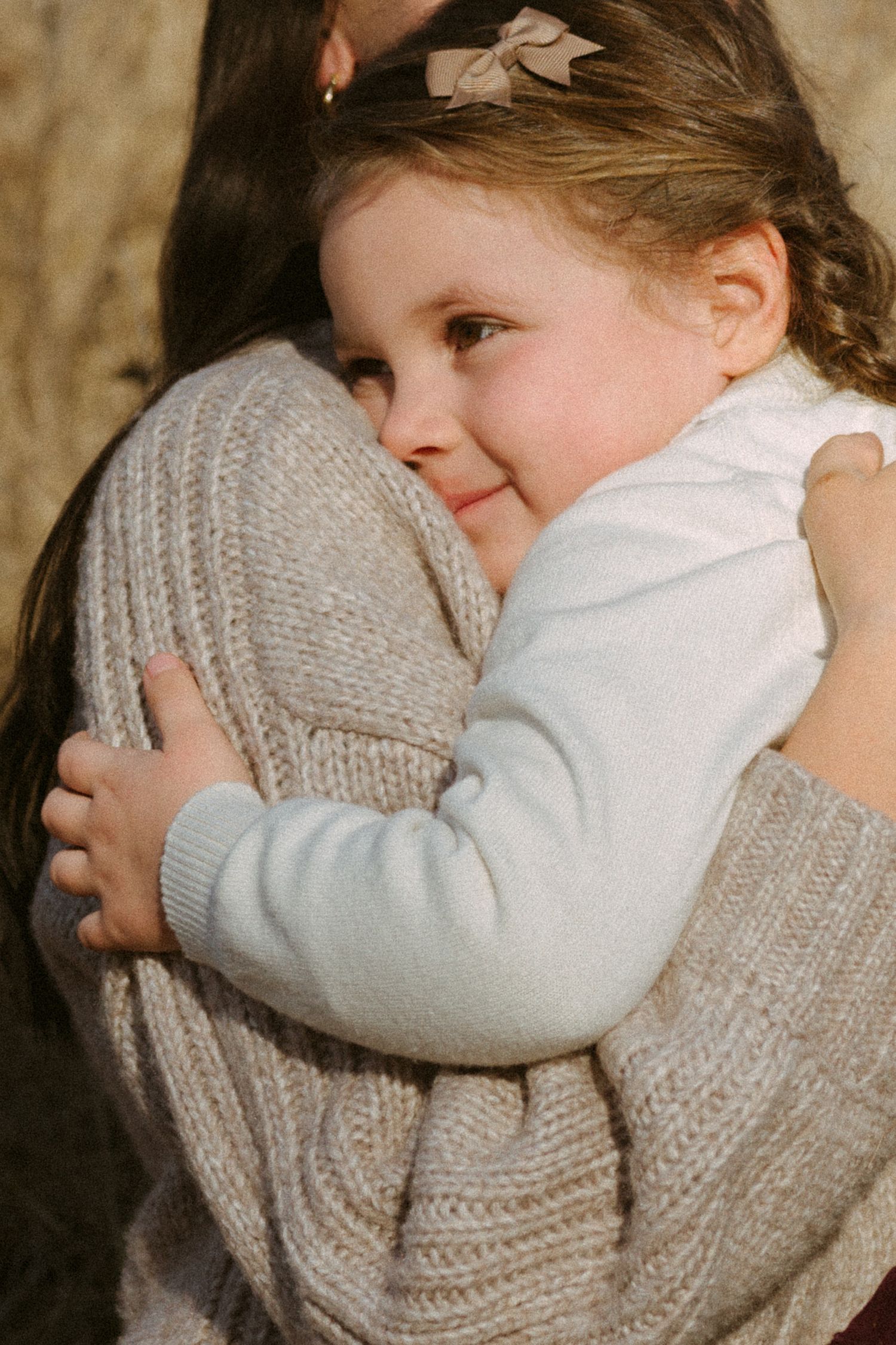 A sweet moment showing a young child in white embracing someone wearing a knit sweater.