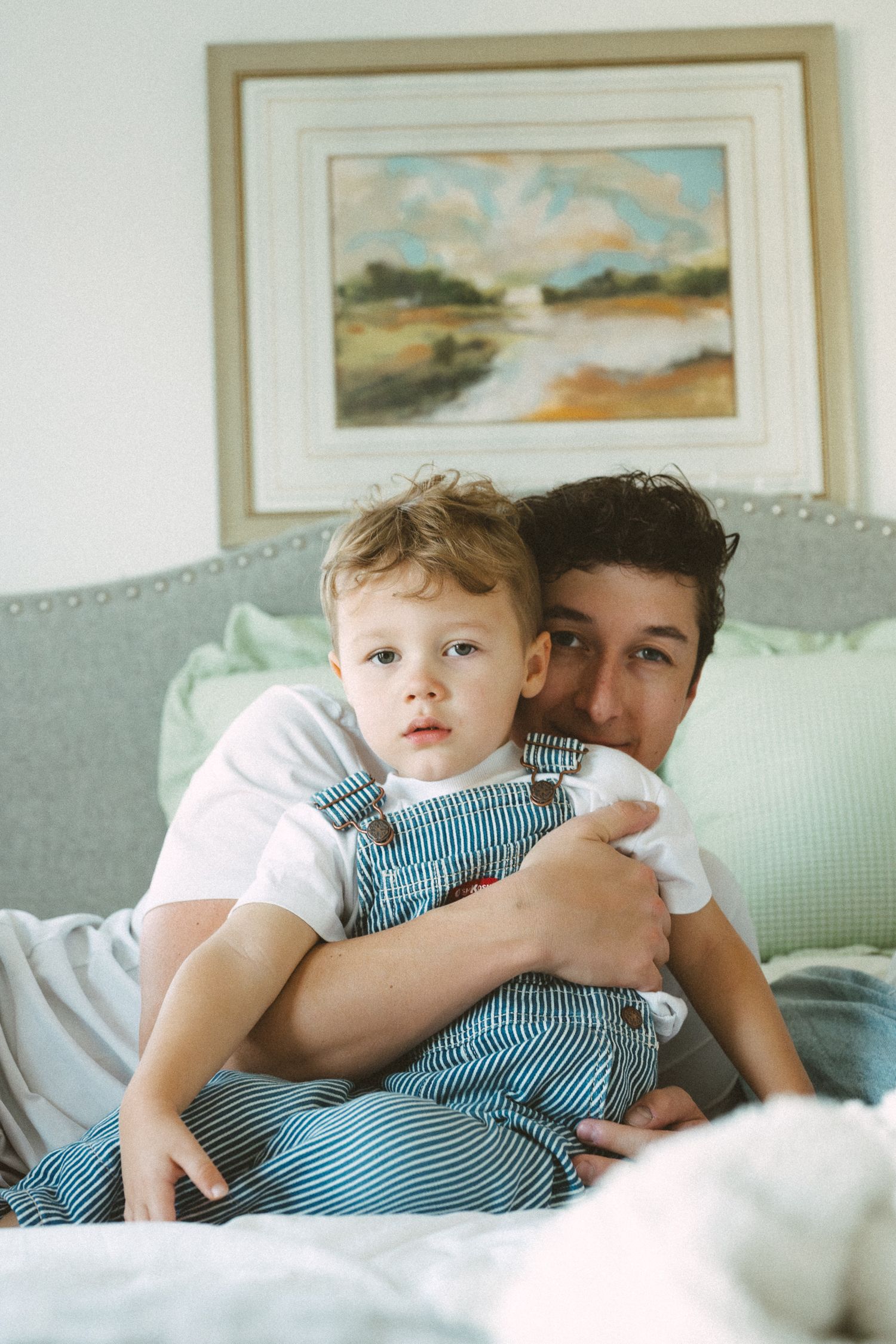 Intimate family moment captured on a light gray couch with soft decor and framed artwork in the background.