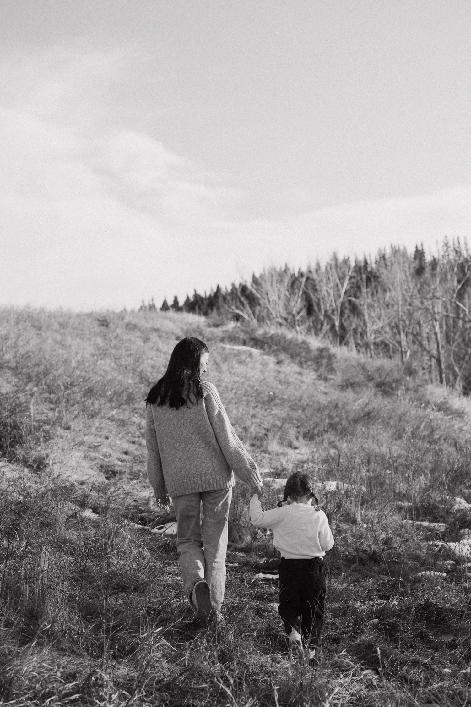 A black and white photo shows two people walking up a grassy hillside together on a cloudy day.