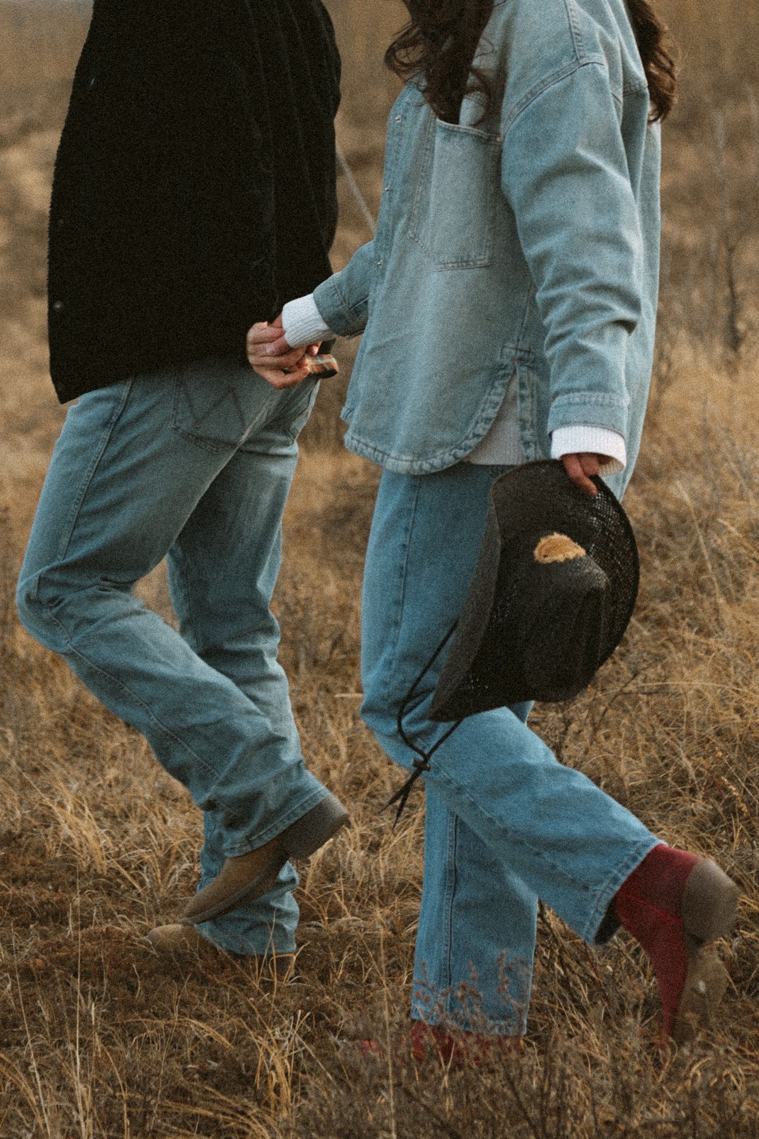 Walking feet in denim and boots through dry grass field.