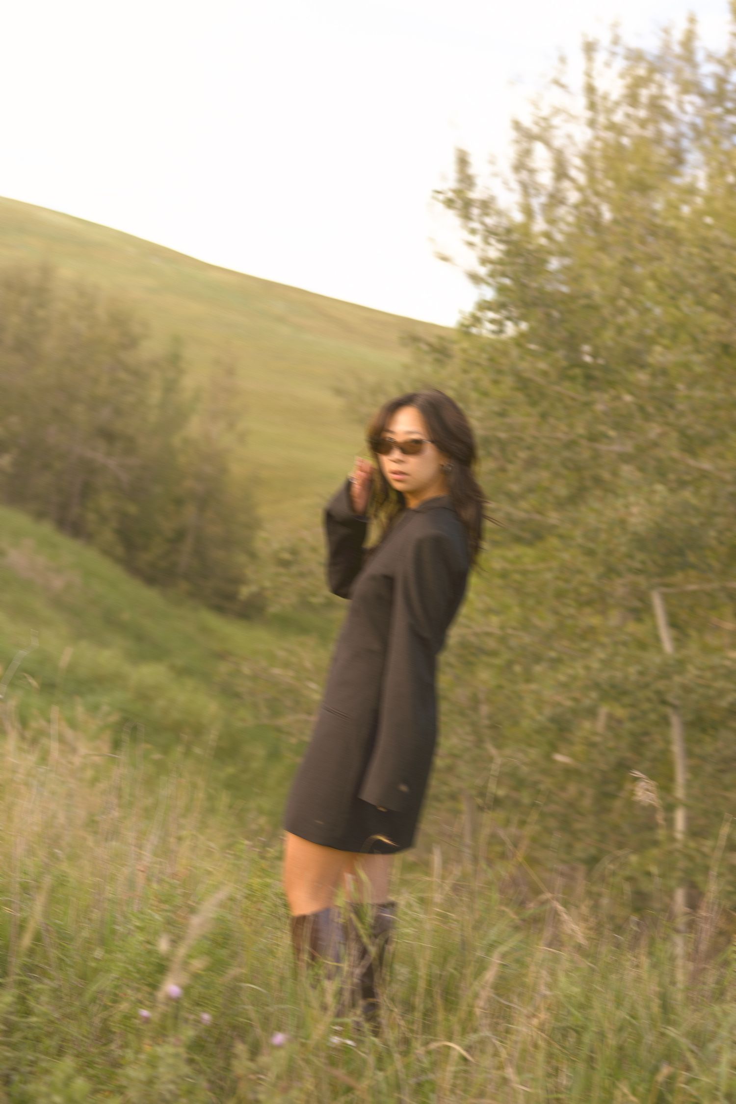 Artistic portrait of someone in black dress standing on grassy hillside.