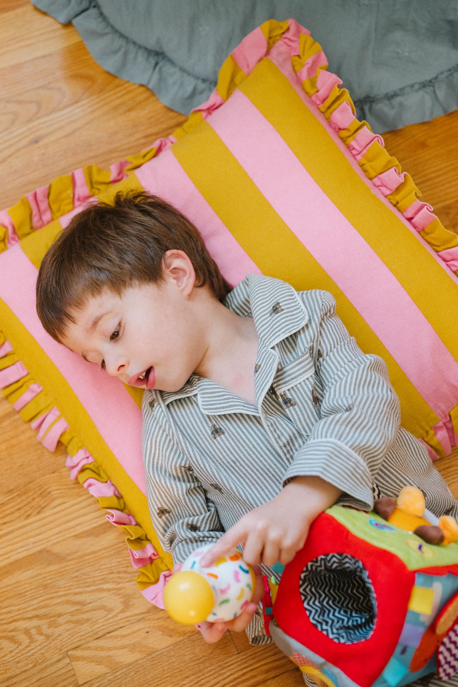 Child lying on striped pink and yellow pillow while playing with red toy.