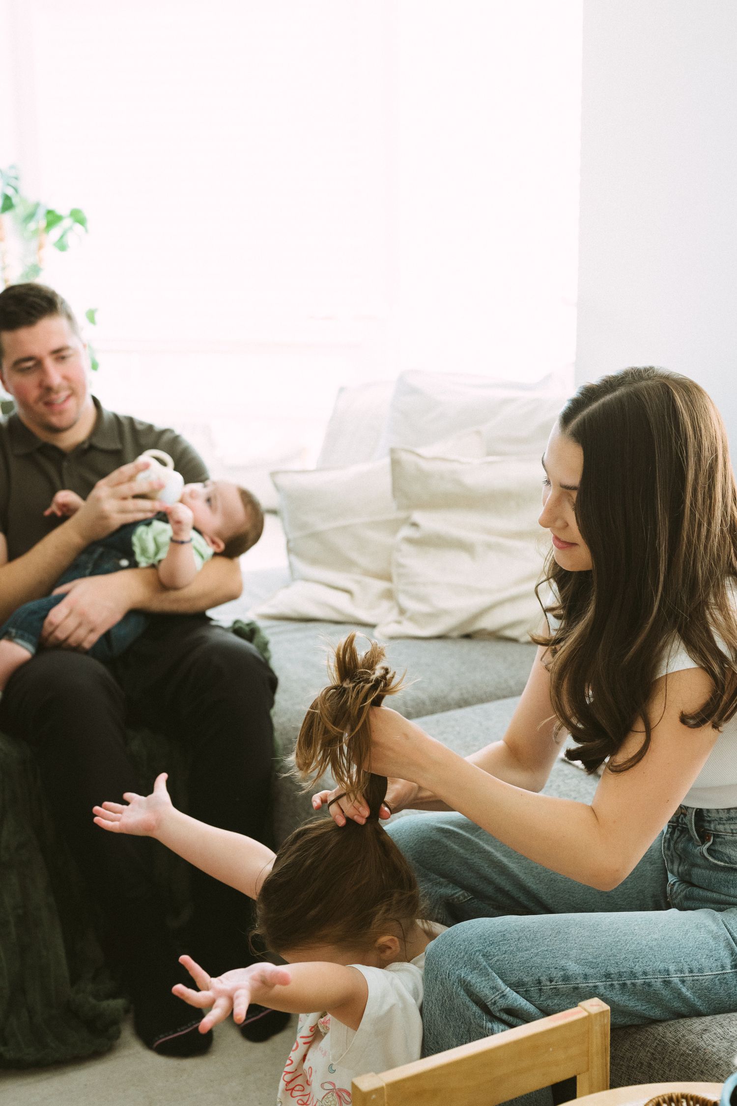 Family members relax together on a comfortable gray couch in a bright living room.