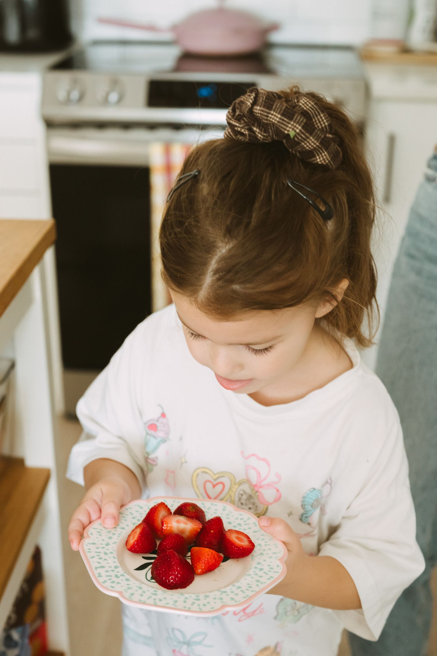 Young child holding plate of fresh cut strawberries in kitchen.