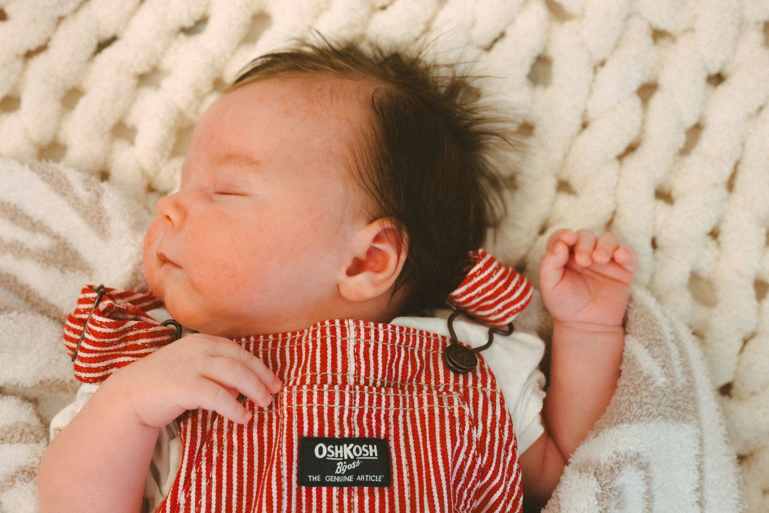 Baby sleeping peacefully on white knitted blanket wearing red striped clothing.