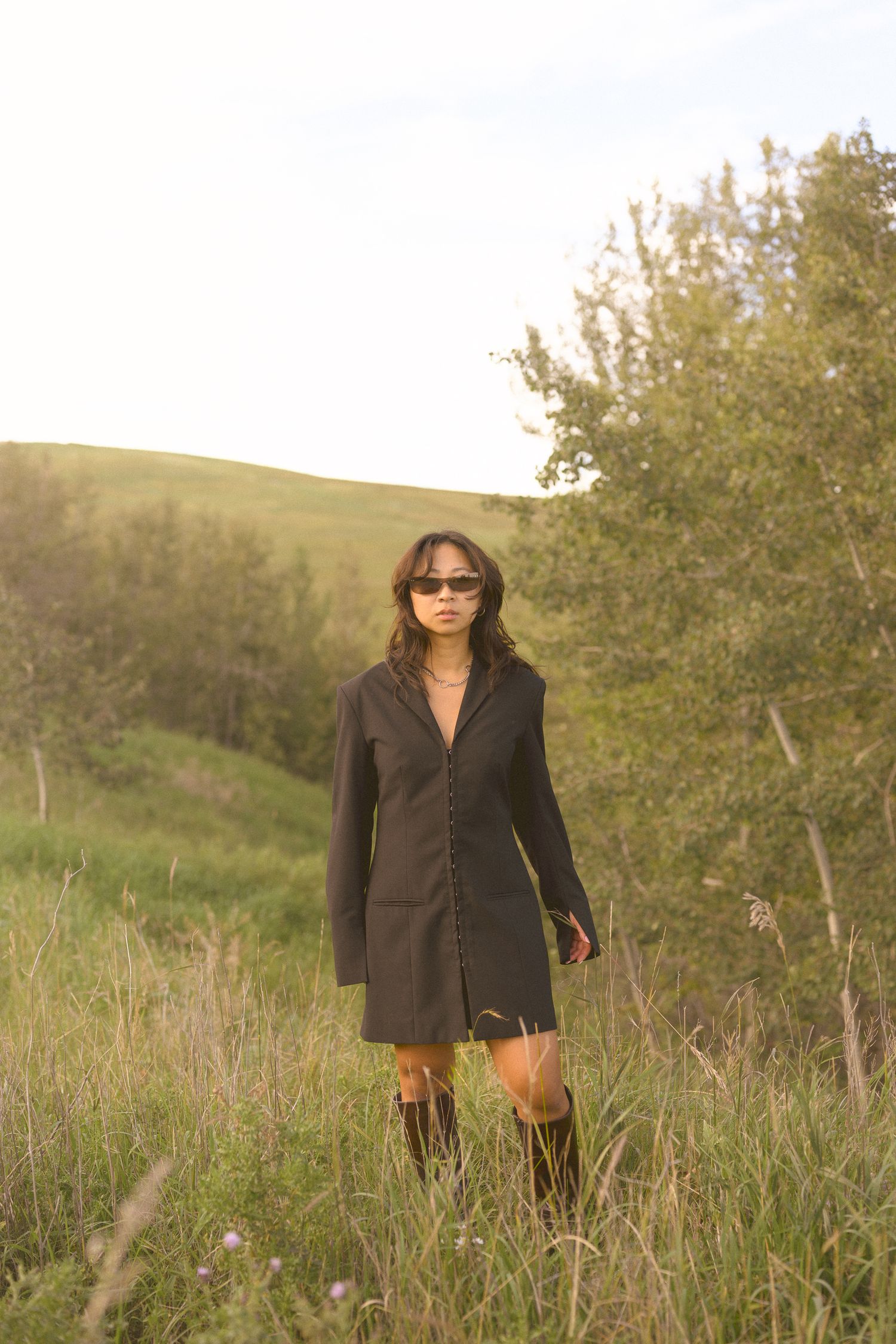 A sleek black coat dress captured in tall grass during golden hour.