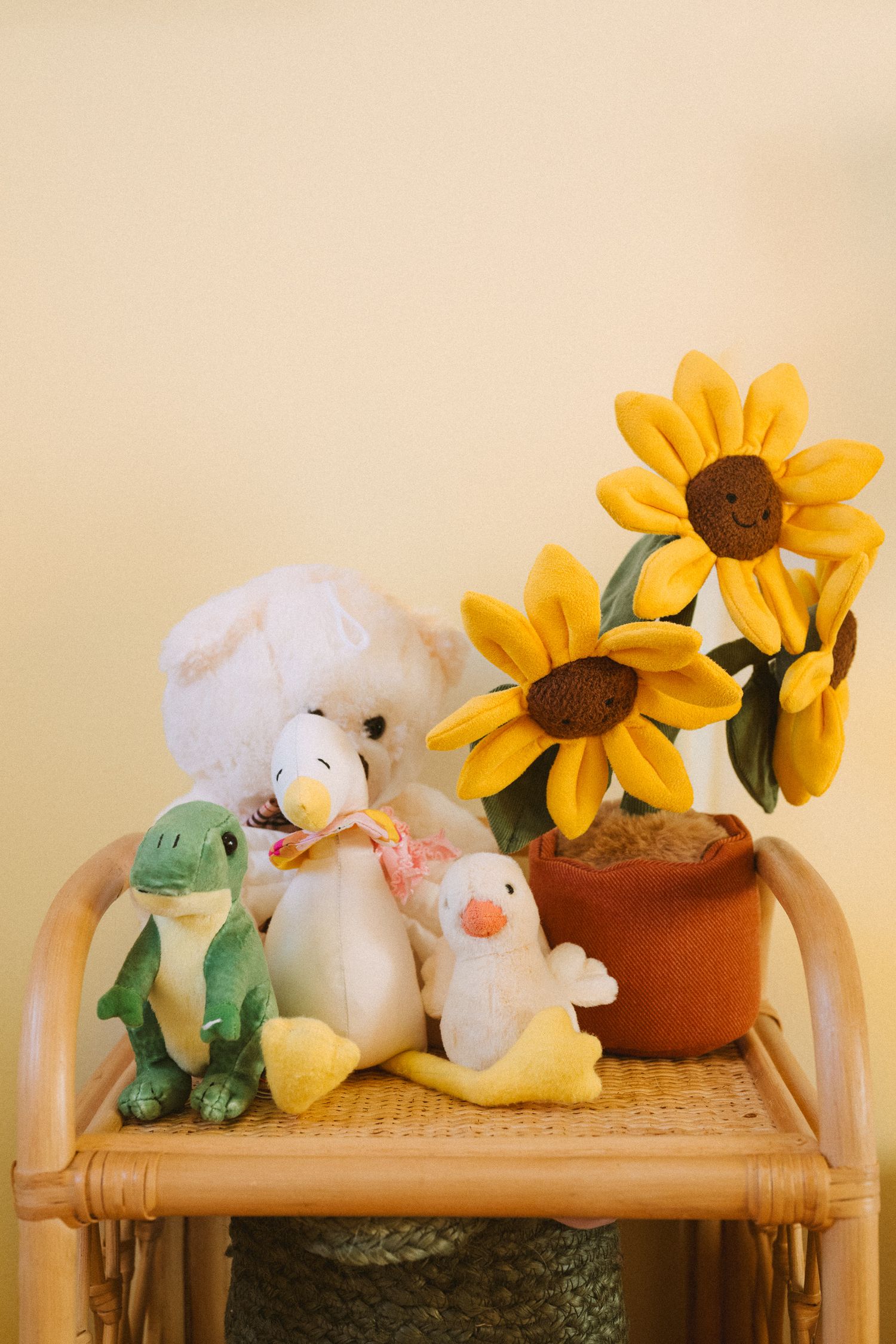 Plush toys and artificial sunflowers arranged on bamboo shelf against beige wall.