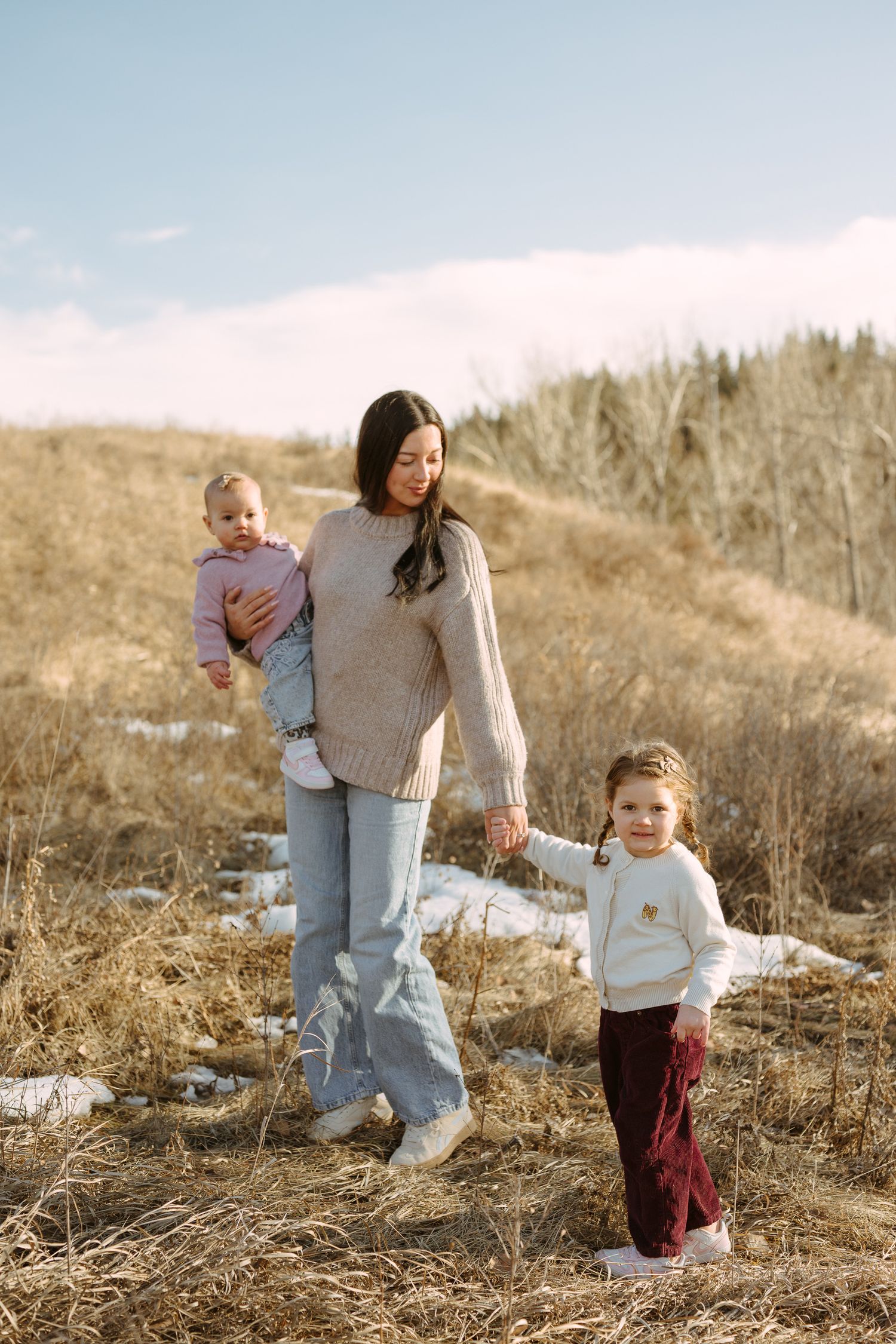 A family shares tender moments together on a grassy hillside during a golden hour photoshoot.