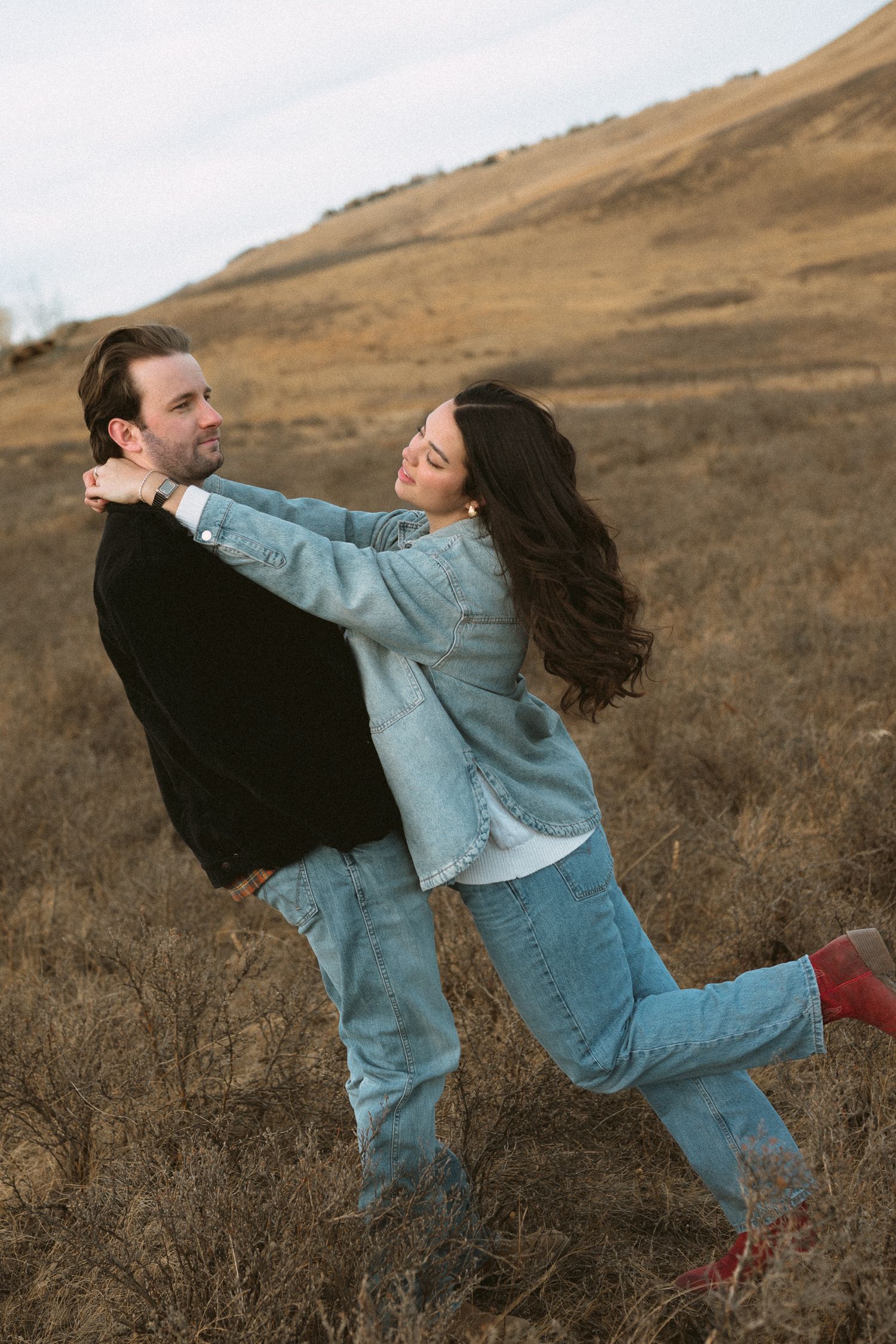 Couple in denim playfully dancing and spinning in a golden autumn field at sunset.