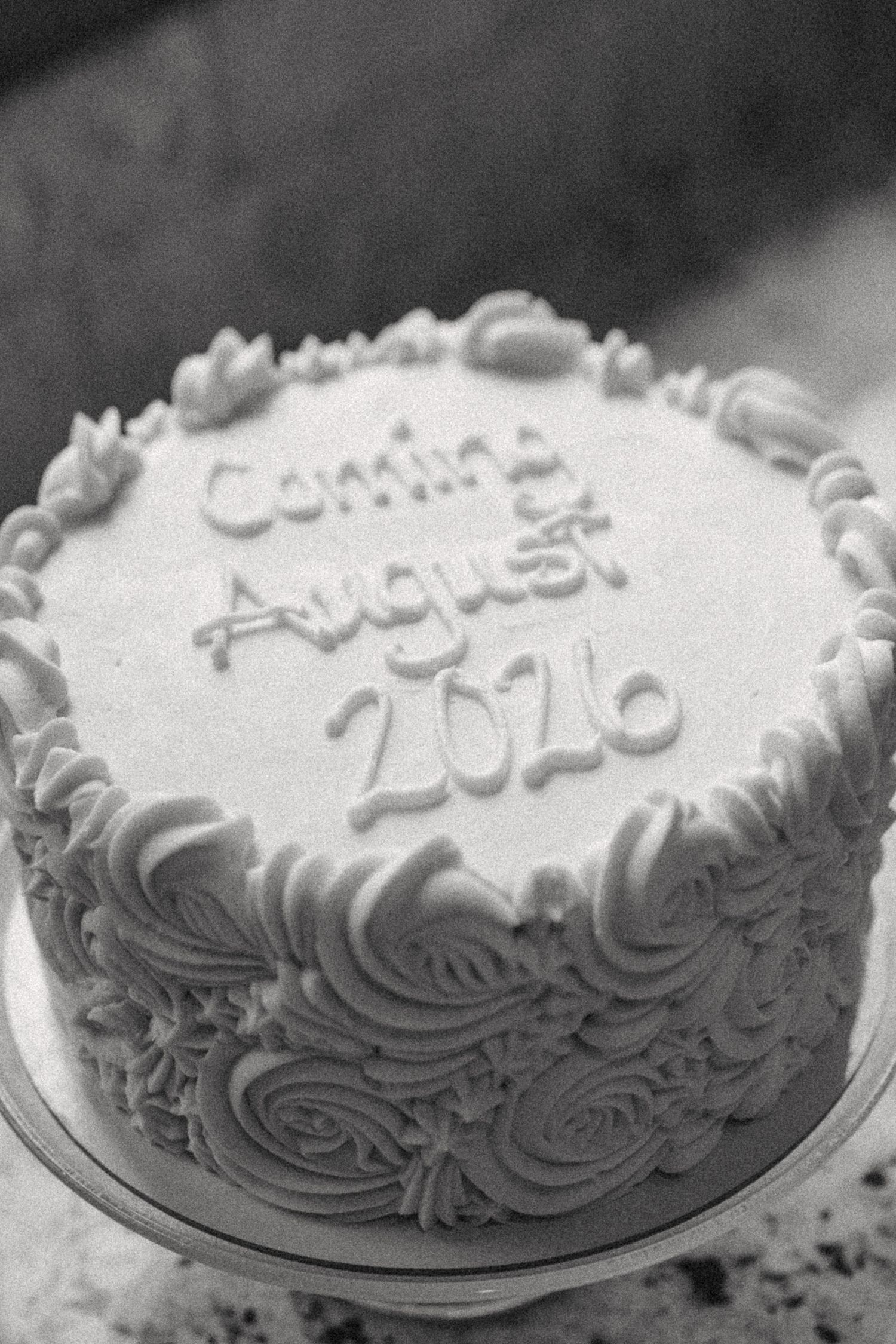 Black and white photo of a decorated celebration cake with frosting roses reading Coming August 2026.