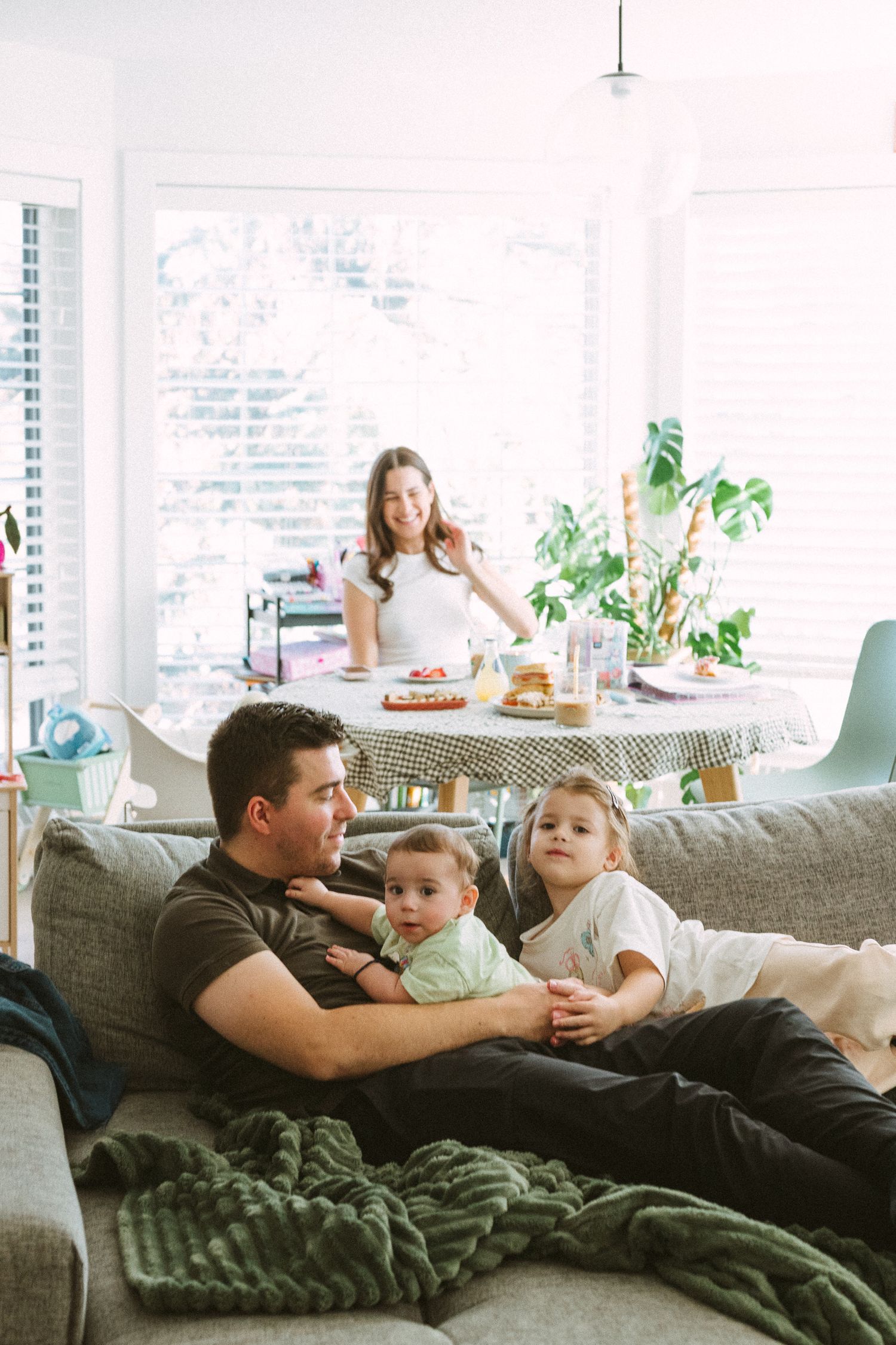 Family relaxing together in bright living room with dining table and houseplants in background.