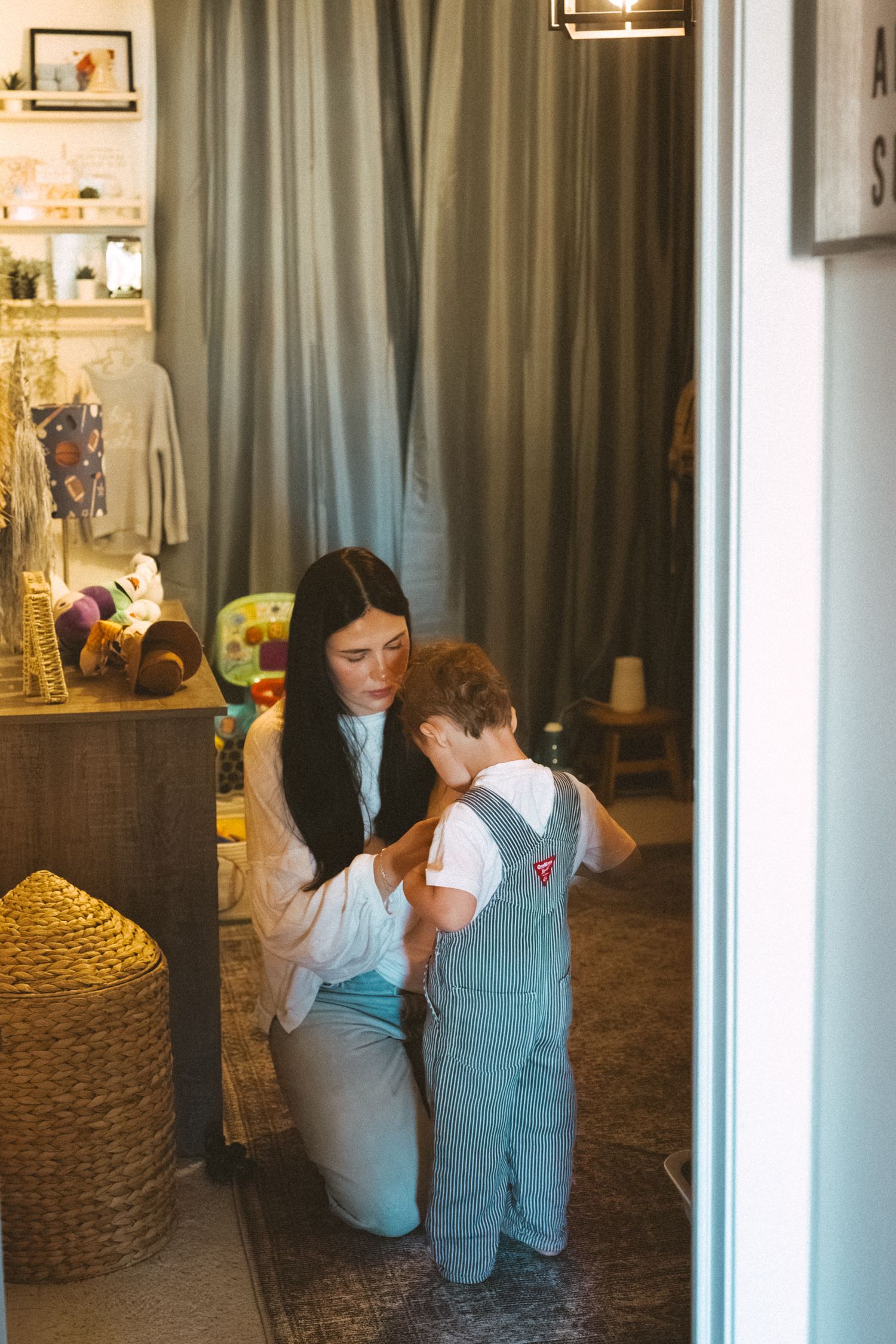 A playful scene unfolds behind sheer curtains in a warmly lit room with woven baskets.