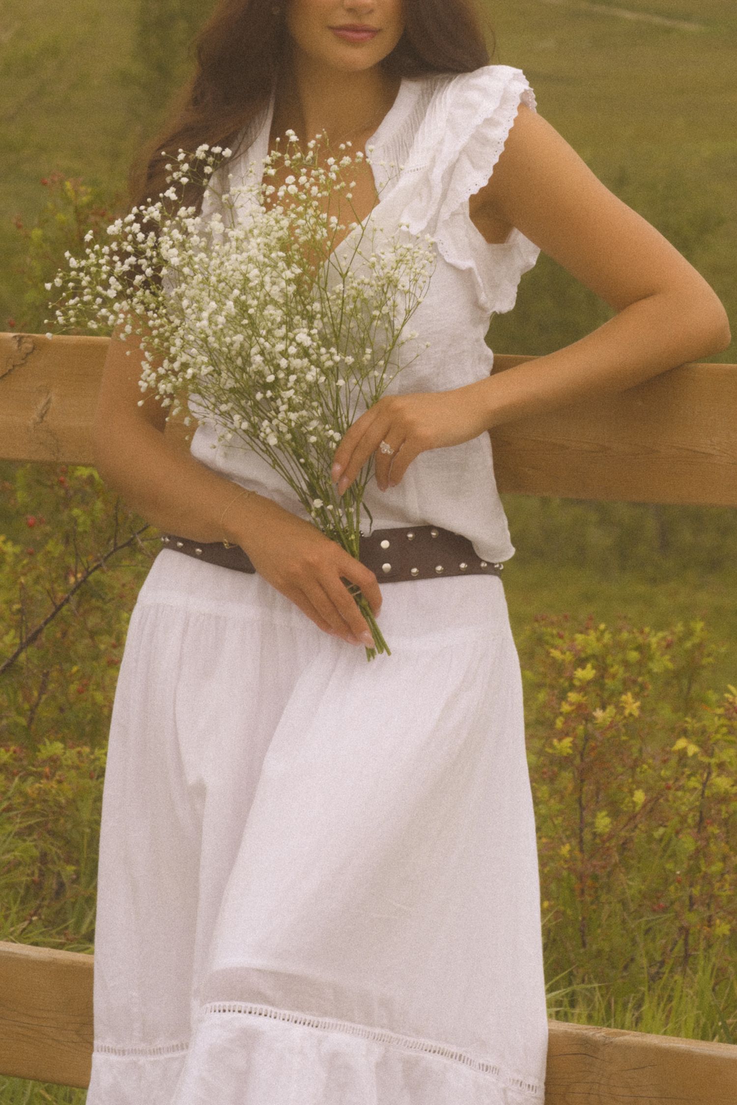 A white summer dress with delicate lace trim and baby's breath flowers creates a romantic countryside look.