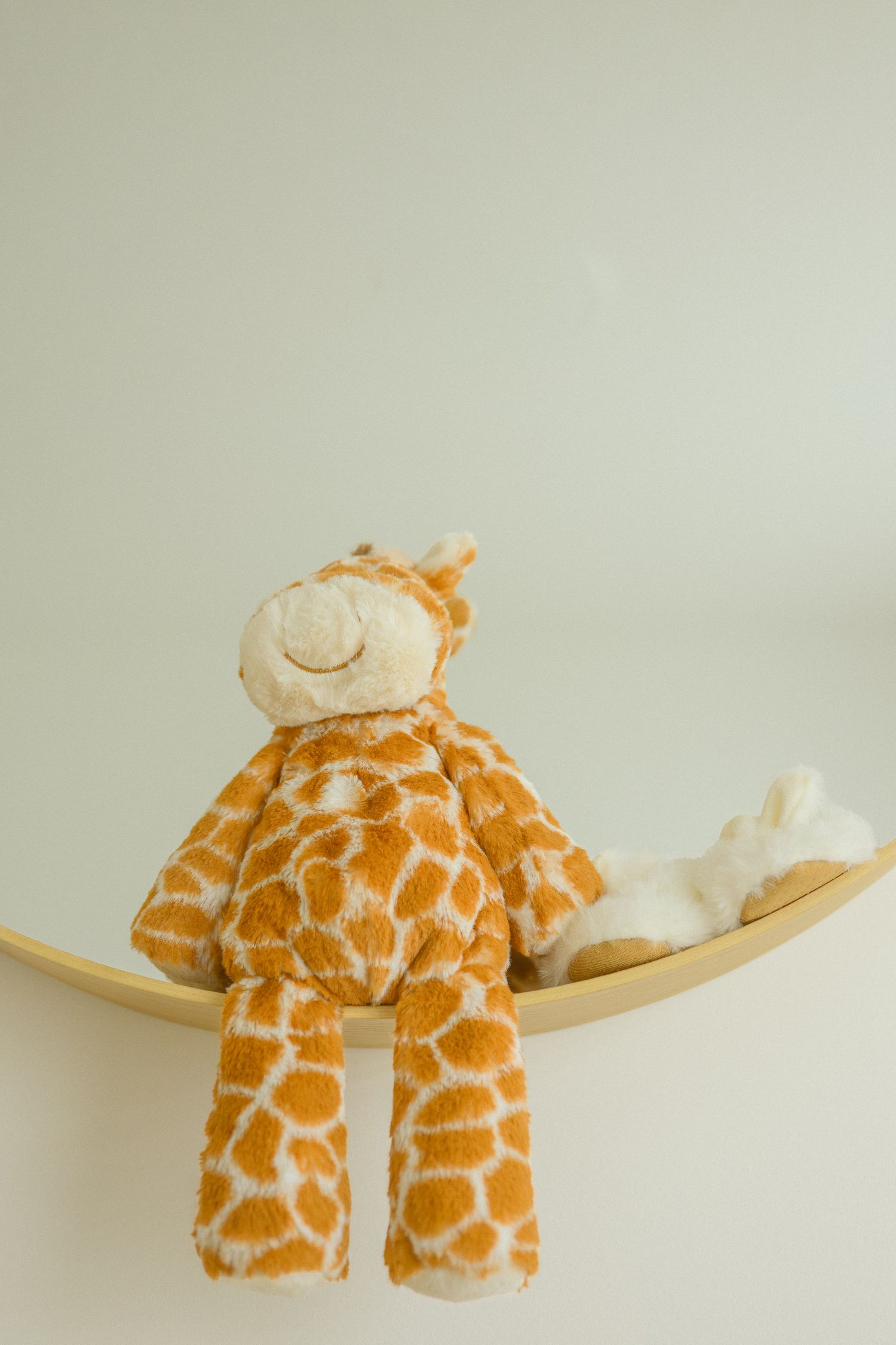 Plush giraffe stuffed animal lying on curved wooden surface.