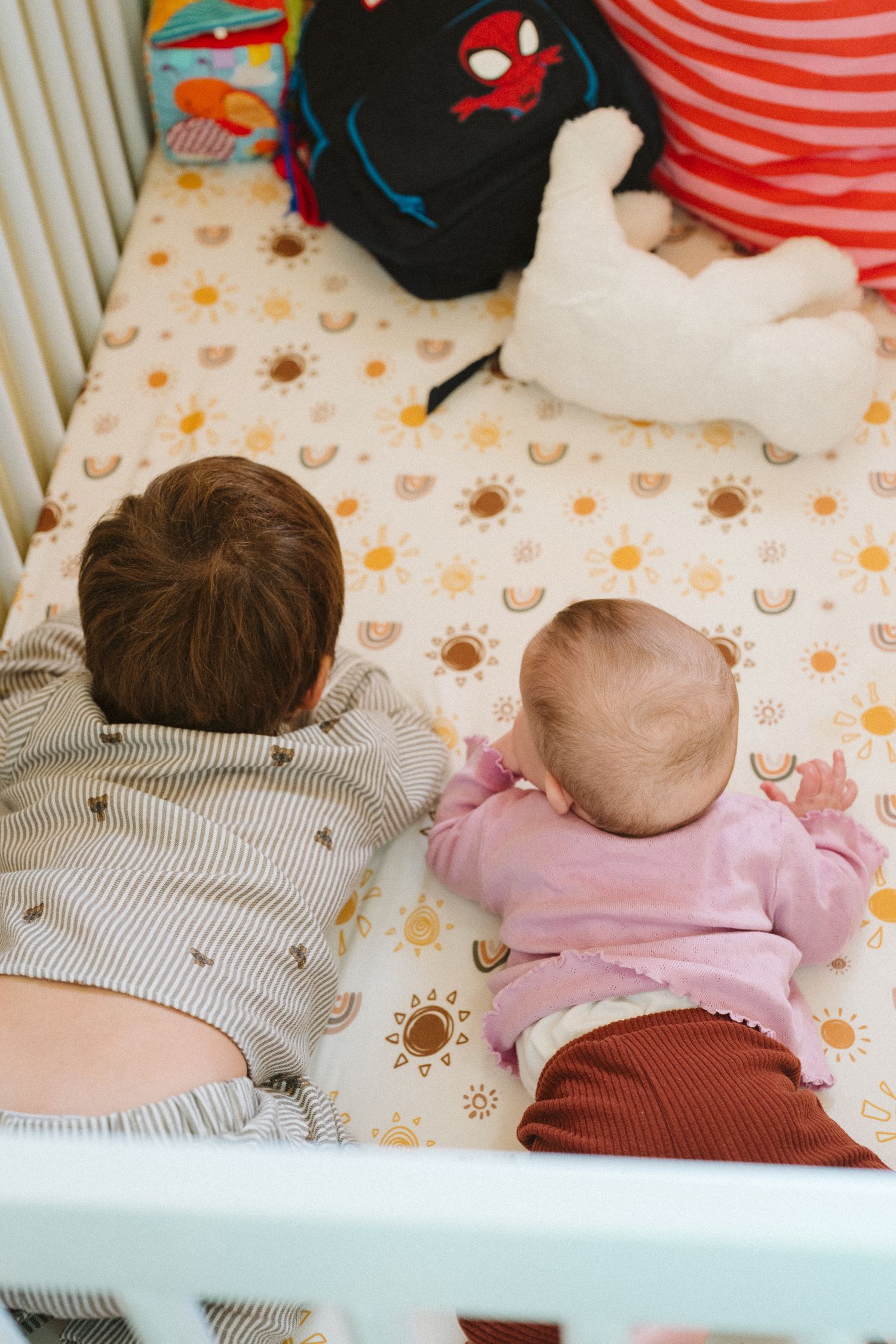 Two children lying together on a patterned bedsheet with sun and moon designs.