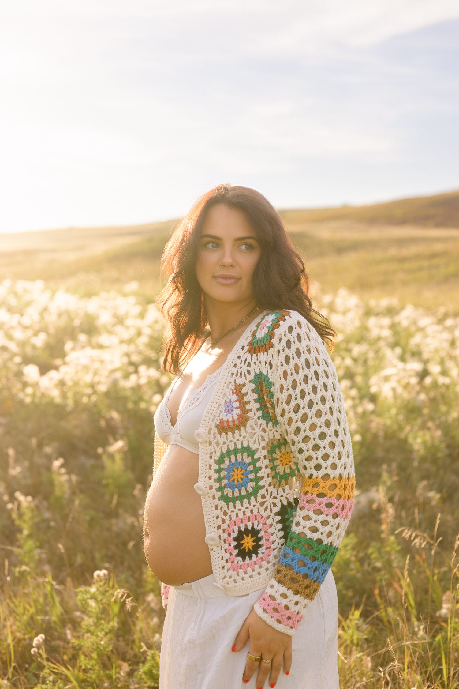 A sun-drenched maternity portrait amid wildflowers with a colorful granny square cardigan.
