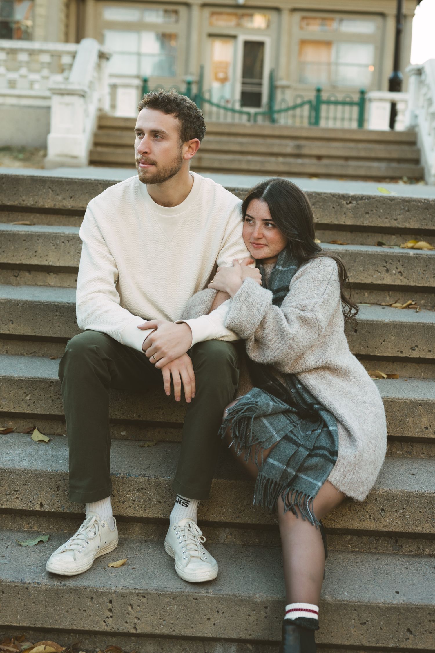 Two people in cozy sweaters share a romantic moment on outdoor concrete steps.