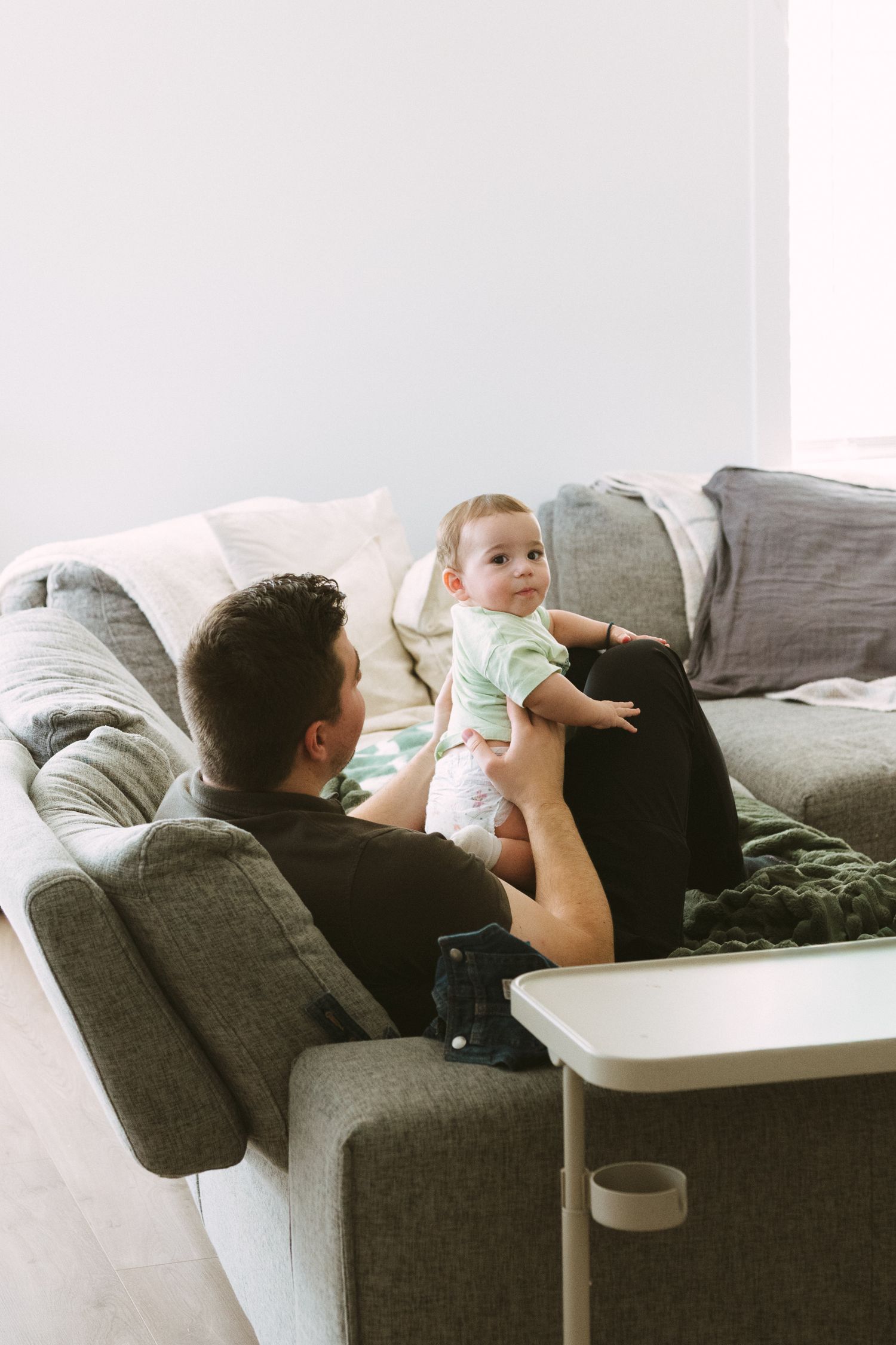 A relaxed family moment on a comfortable gray sofa with a small child being lifted up playfully.