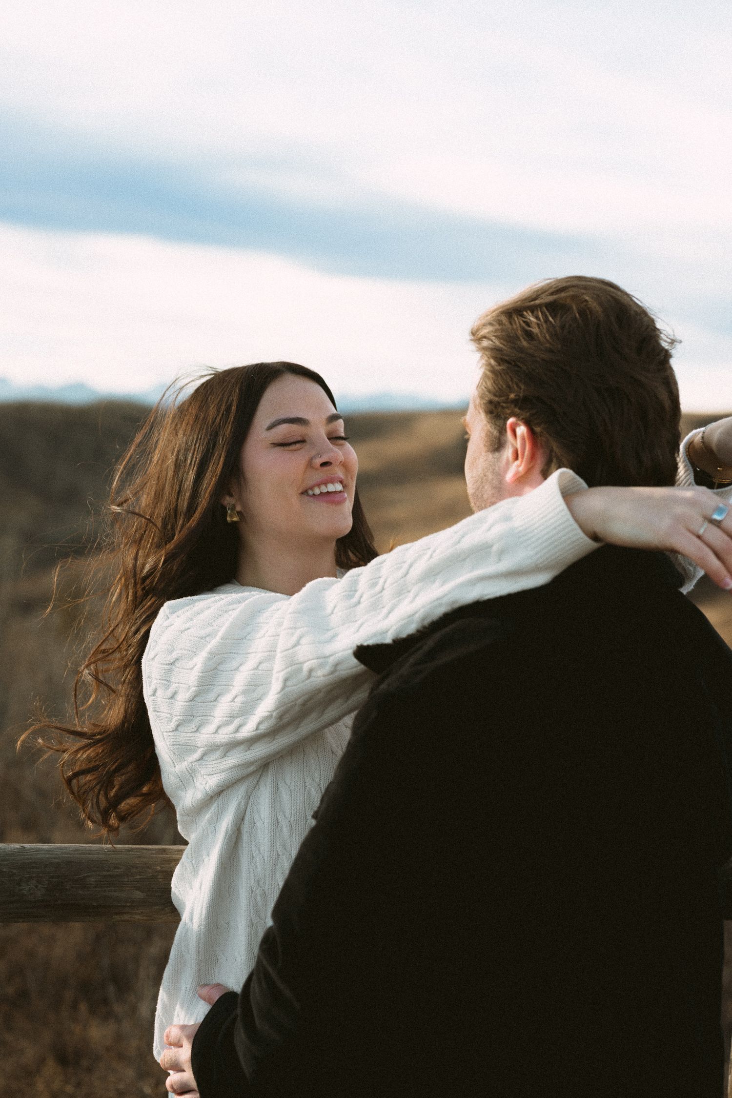 A romantic embrace captured in profile against an overcast sky in a rustic outdoor setting.