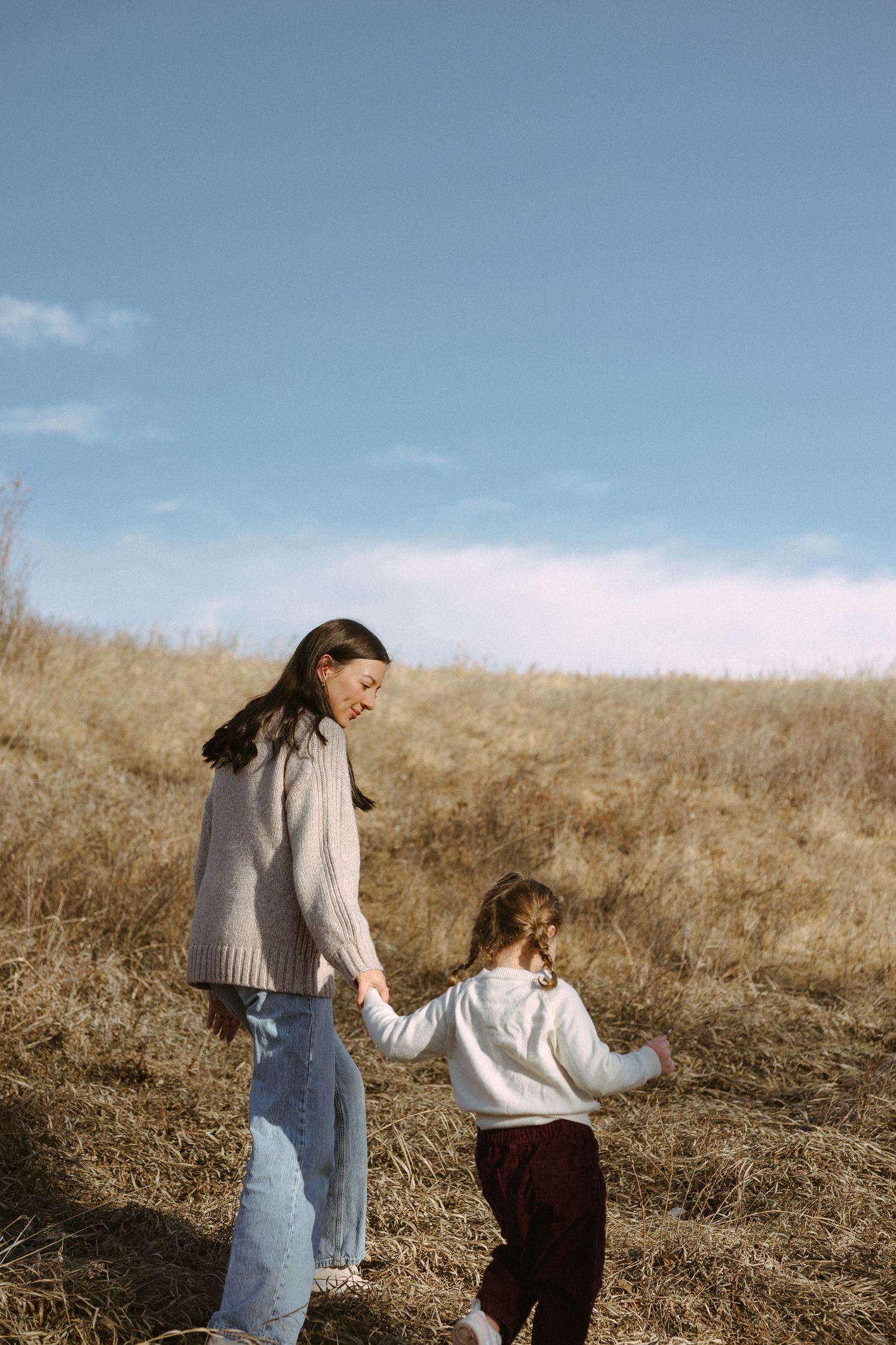 Two people walking together through a golden grassy field on a sunny day with blue skies.