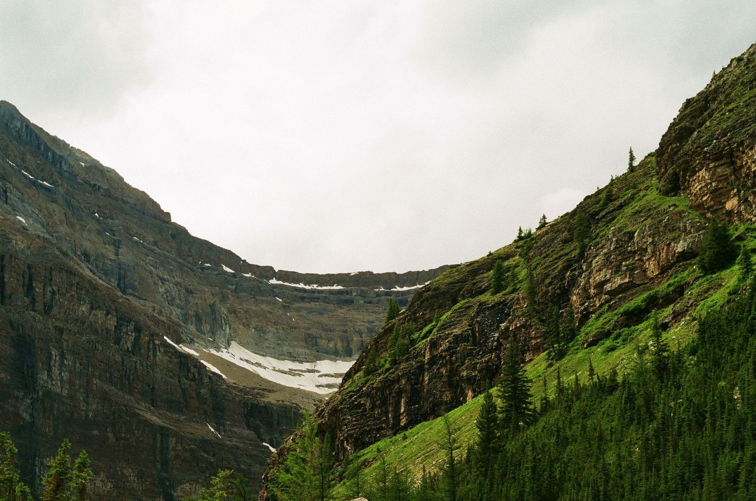 Snow-capped mountain peaks rise above green slopes in a dramatic alpine landscape.