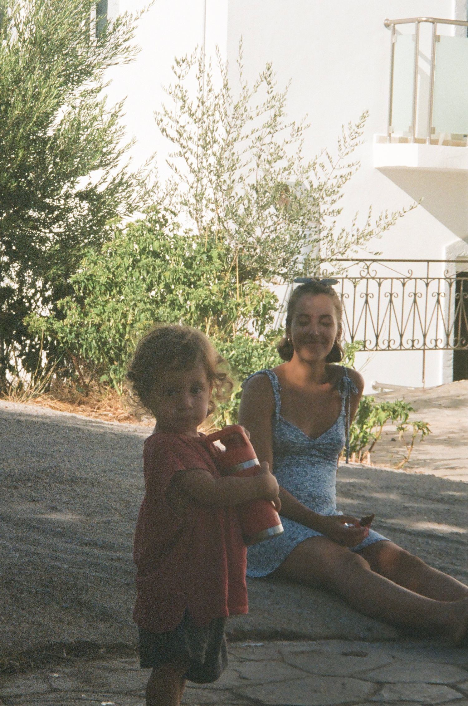 Children and adults sitting together outdoors in a casual setting near some greenery.