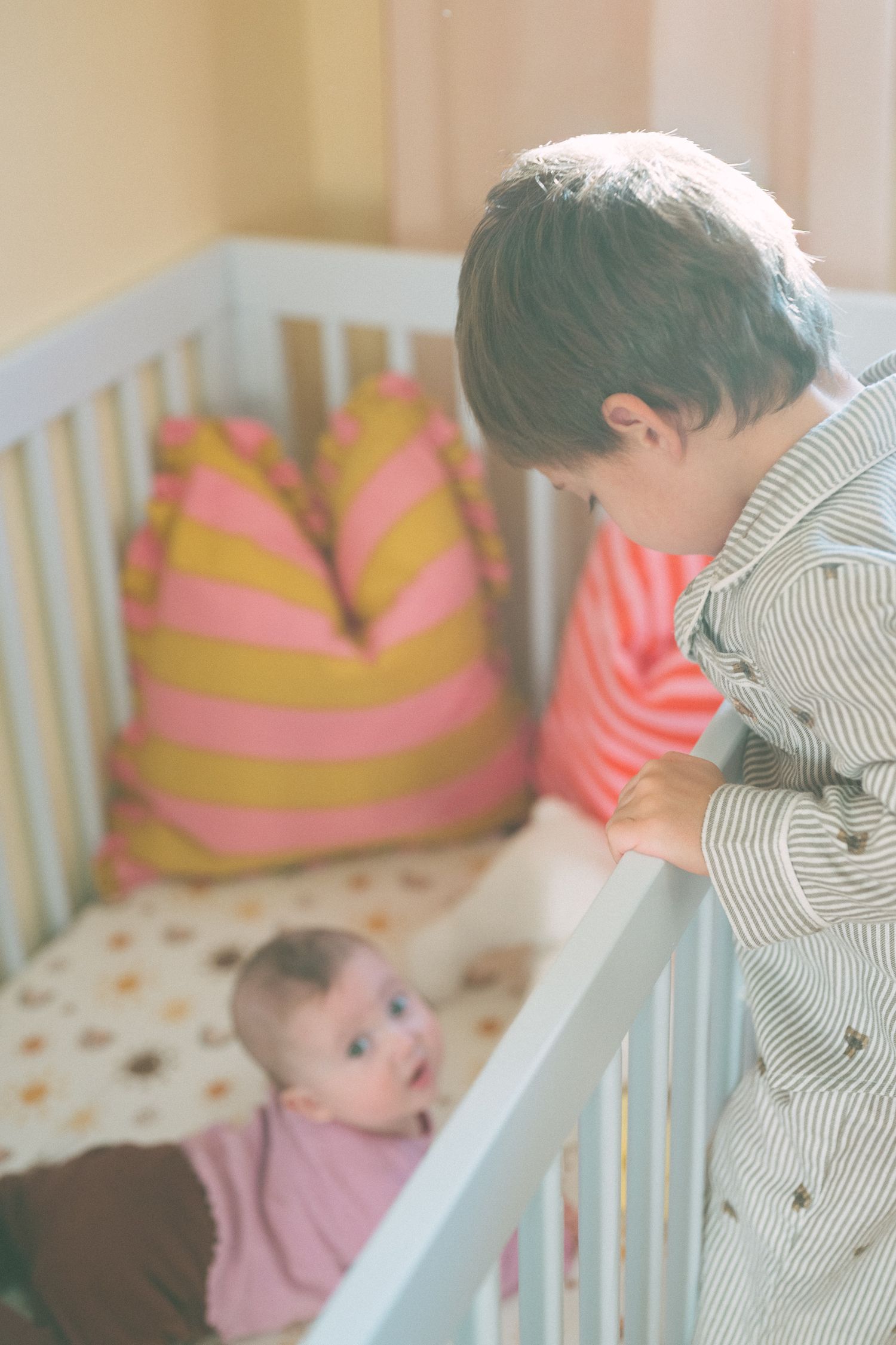 White crib with pink and yellow striped pillows in sunny nursery.