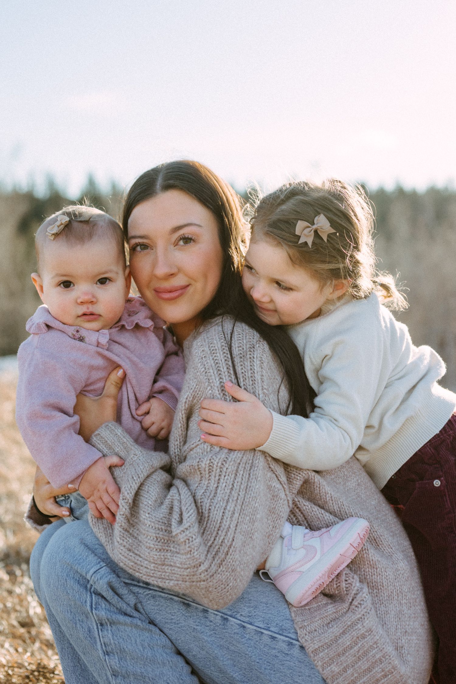 A tender family moment captured in warm sunlight with mountains and trees in the distance.