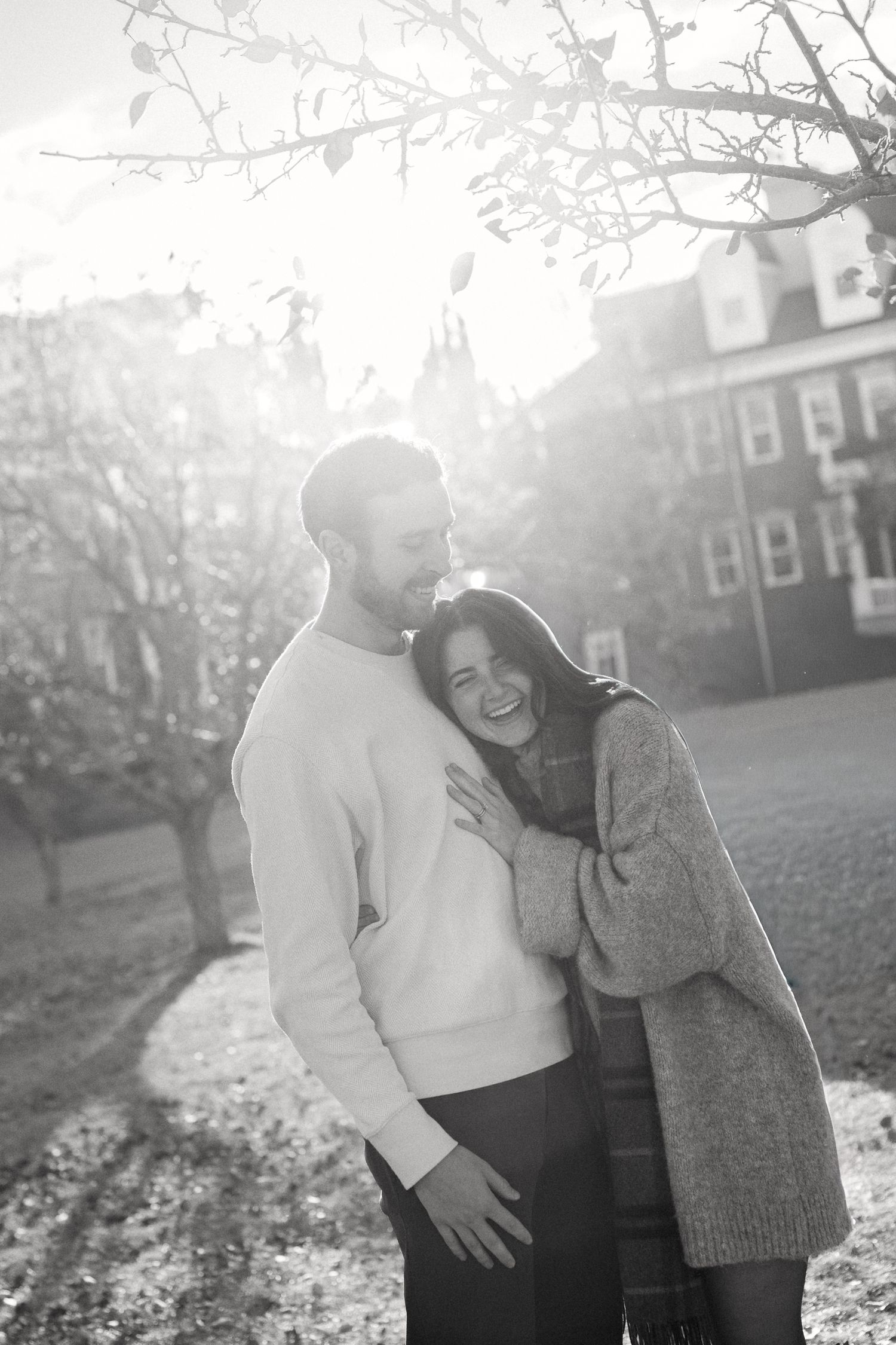 Couple sharing intimate moments in a sunlit park with brick buildings in the background.