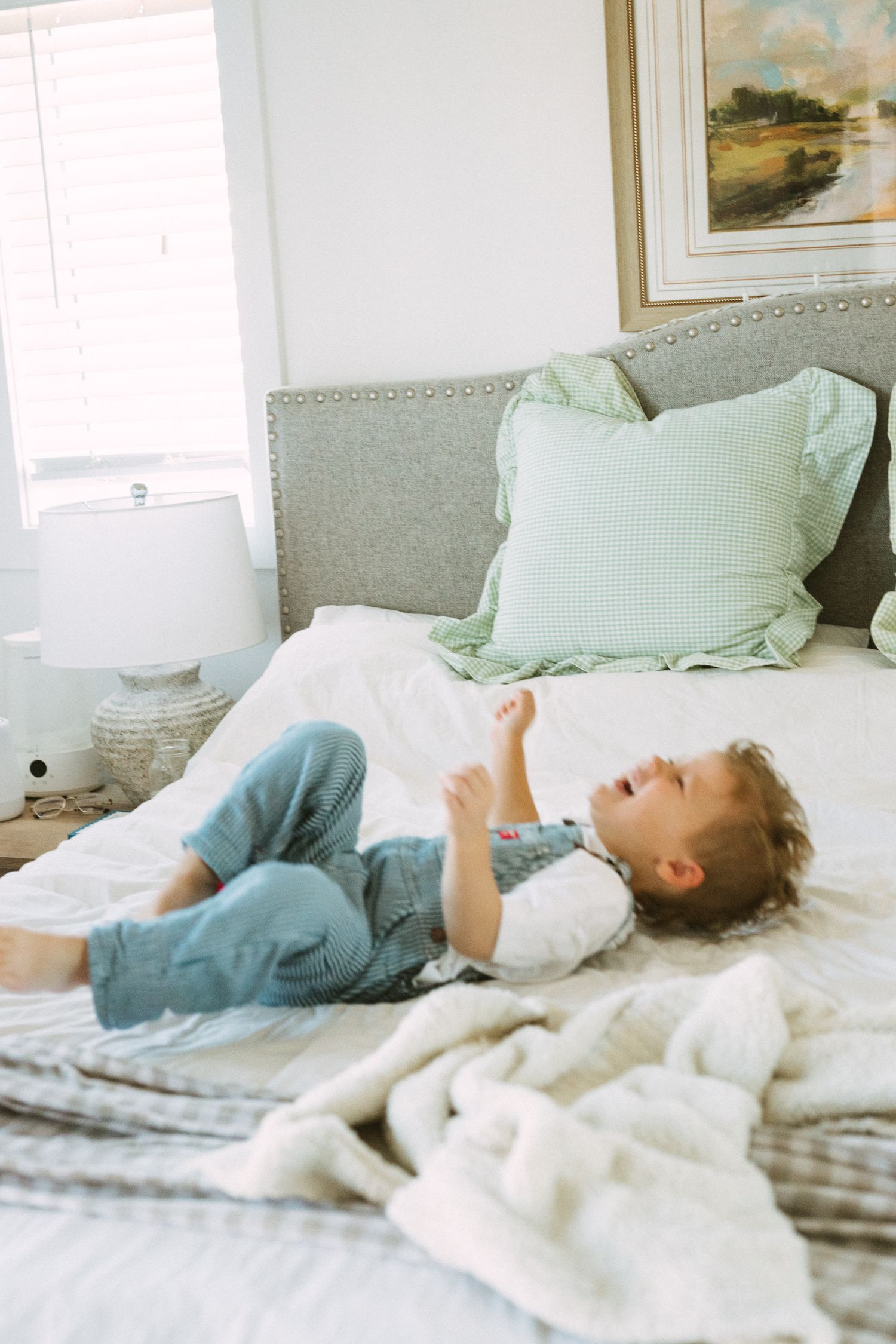 A young child relaxes on a plush bed with mint green pillows and white bedding.
