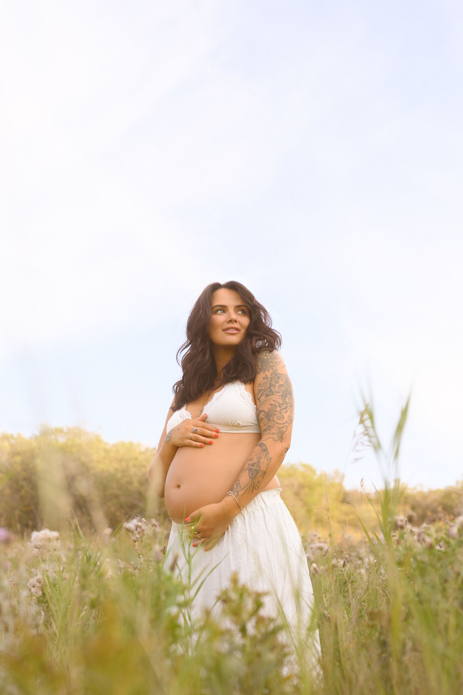 Intimate maternity portraits taken in a wild flower field during sunset with soft natural lighting.