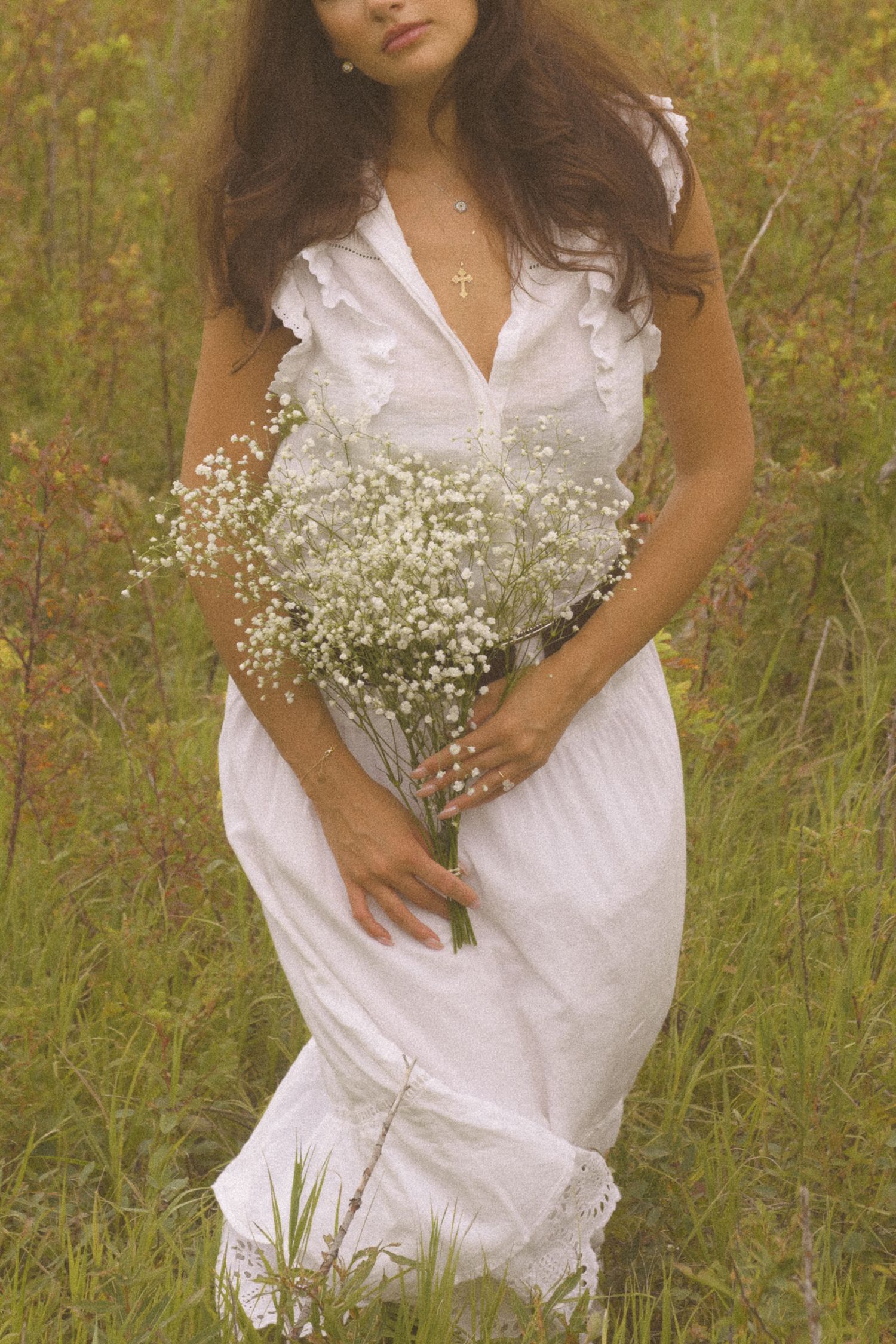 Person in white dress holding delicate baby's breath flowers in a summer field.