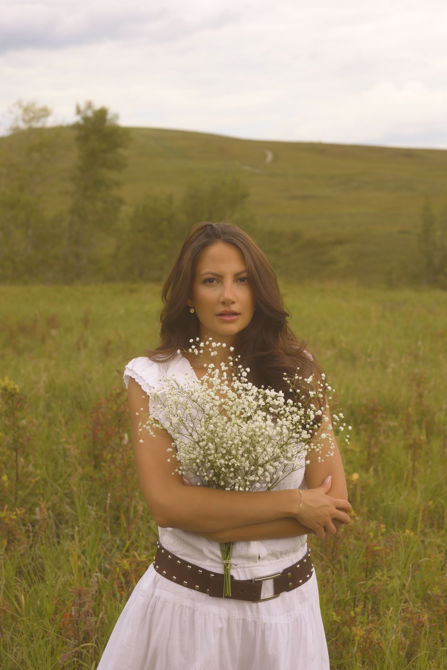 A person clutches white baby's breath flowers while posing in a summer meadow.