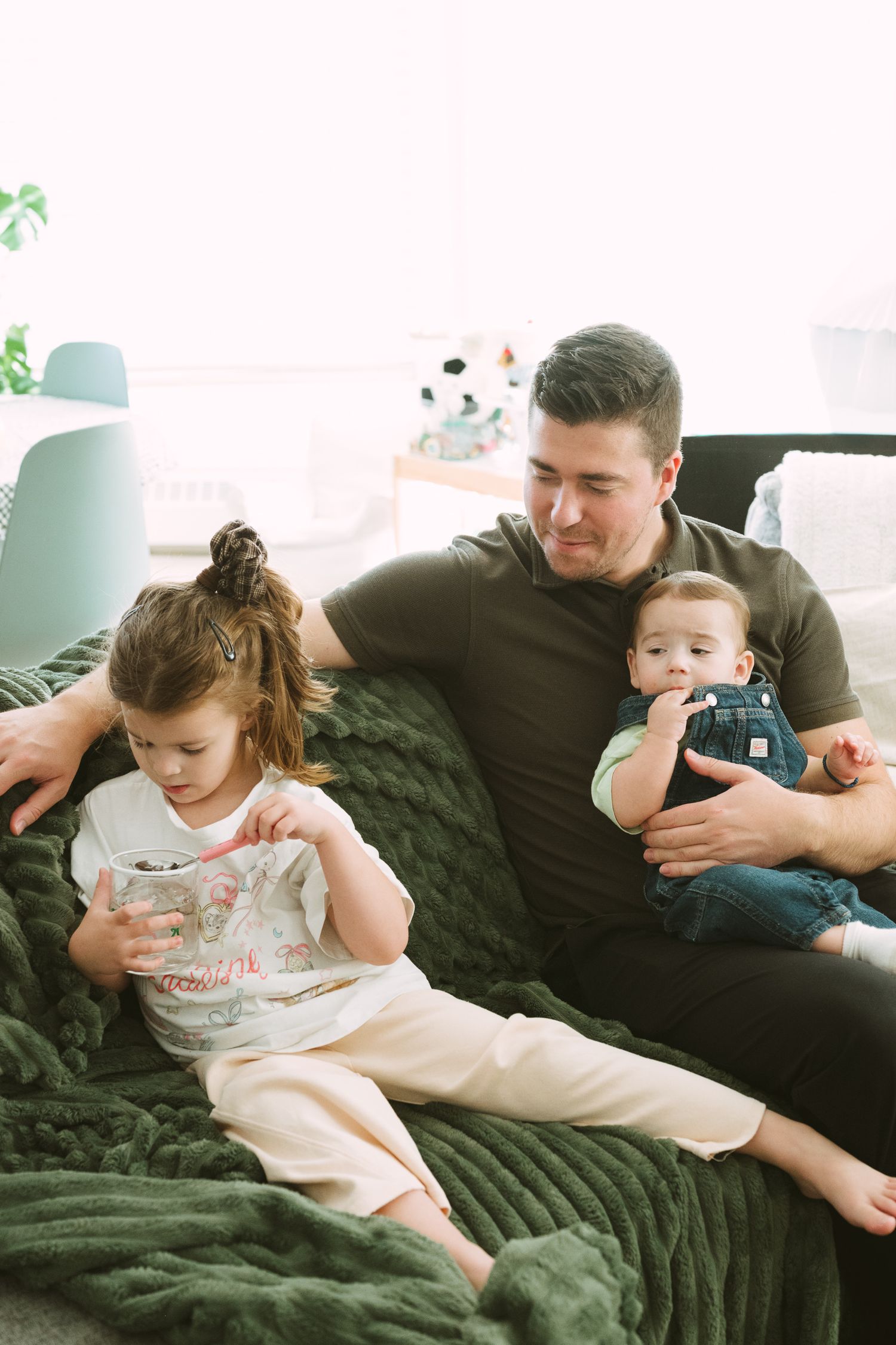 Parent and child relax together on a dark green couch while looking at a mobile device.